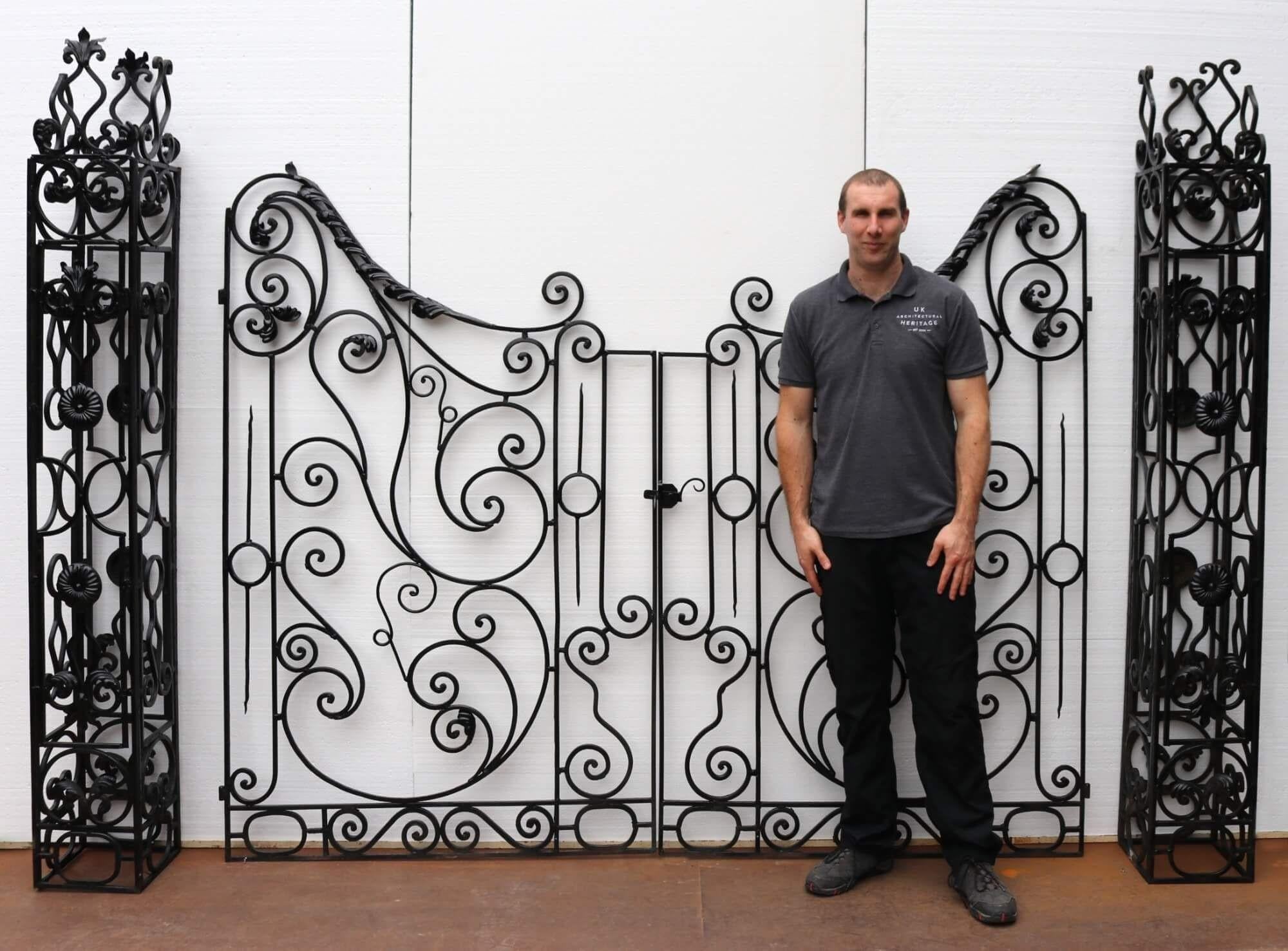 Blacksmith-made in the mid 20th century, this set of tall wrought iron driveway gates with accompanying posts are beautifully handcrafted with timeless scrolling details and unusual sweeping arches. These antique driveway gates originate from France