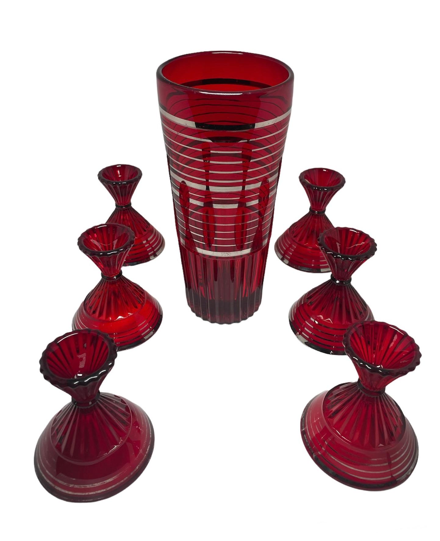 This is a set of a Ruby red glass and silver cocktail shaker and six Martini glasses. The shaker is shaped as a tall cylinder and decorated with silver bands. The decoration in the bottom part is ribbed giving the shaker an special look, The glasses
