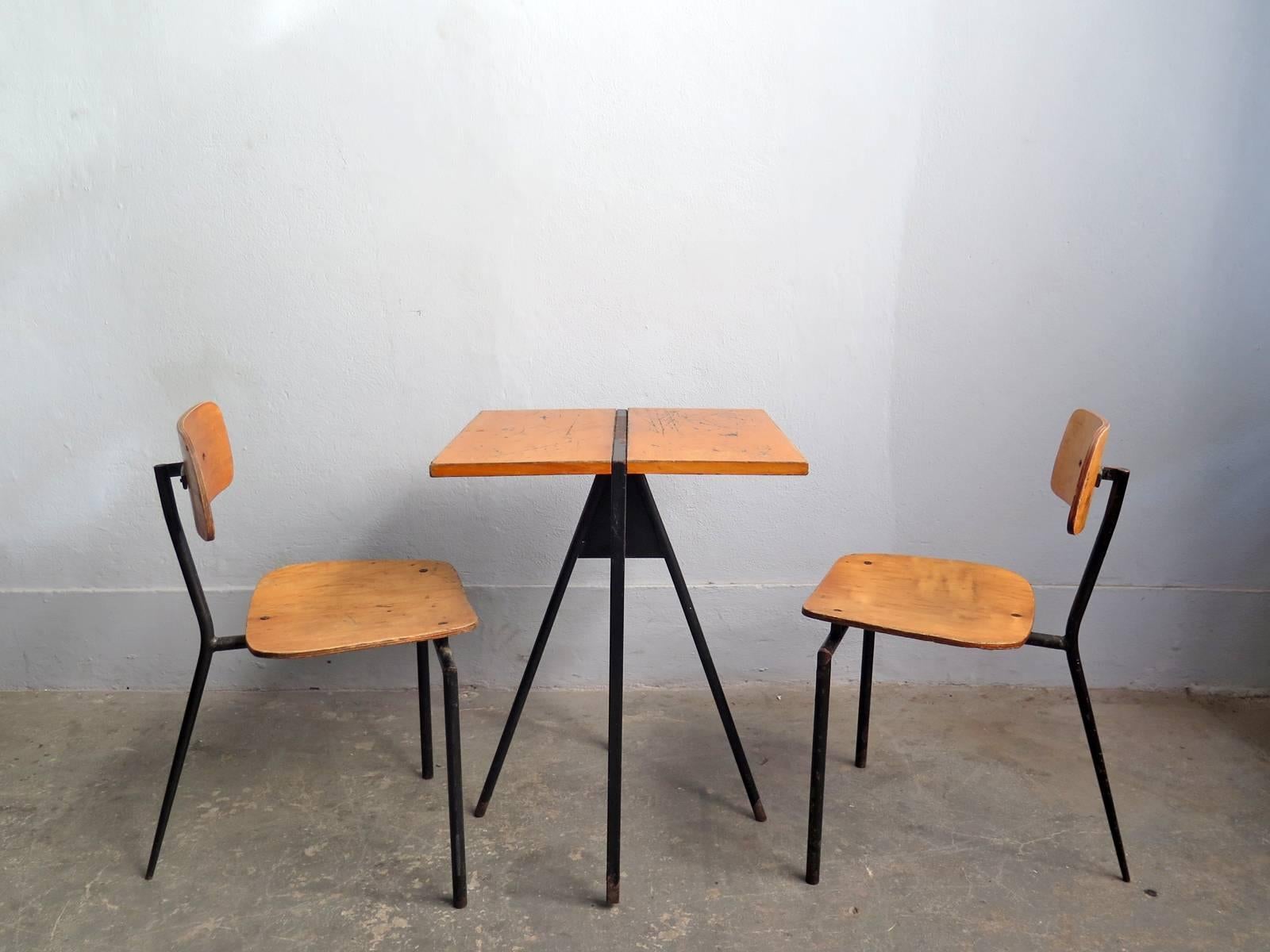 Set of two three-leg chairs and bistro table from with black painted metal frames and wooden parts.