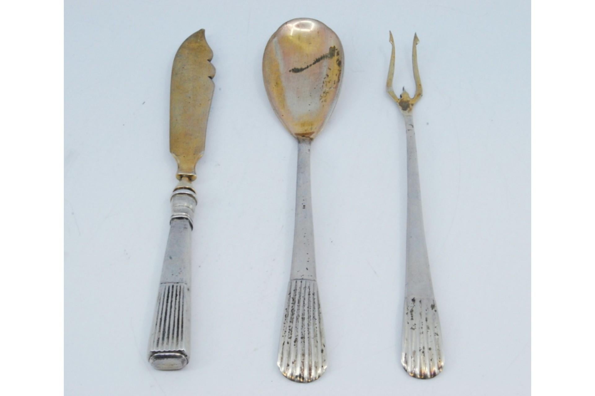Description: Set of pickle fork, butter knife and sauce spoon in gold with fluted handles. Metal: Silver. Origin: Portuguese. Brand: Cabeça de escravo. Weight: 166.96 grams (Set of three pieces). Dimensions: Spoon - 18.5x3.6cm. Content: 833/1000.