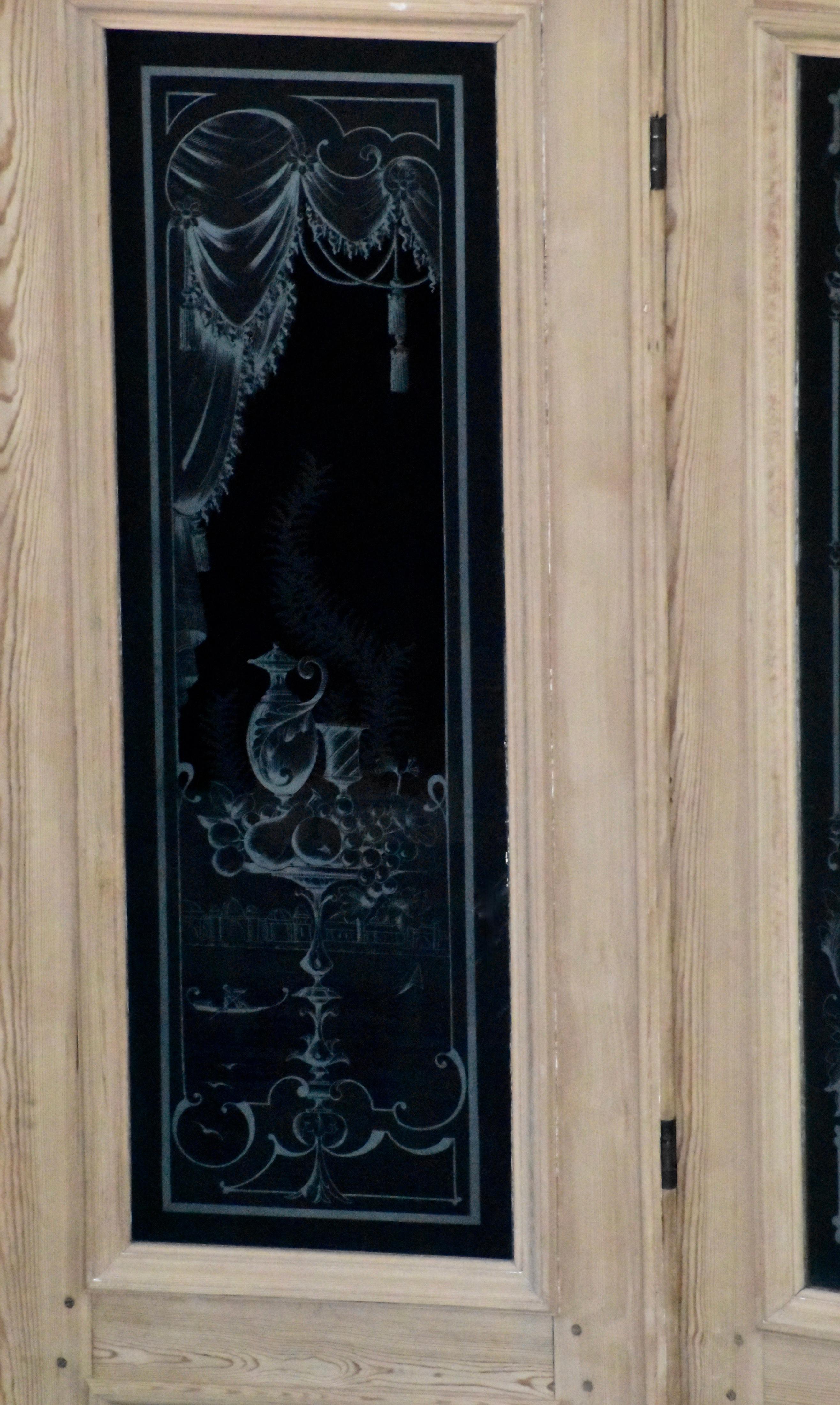 Ce magnifique ensemble de portes est illustré avec un fond noir derrière le verre gravé pour mettre en valeur les détails. Le verre des deux portes extérieures présente une carafe, un verre et des fruits sur une petite table avec un fond de bateau.