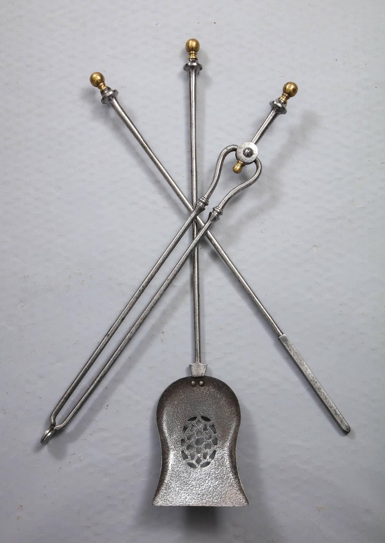 A set of firetools in polished steel comprising shovel, poker and tongs, the shaped shovel with oval piercework centre, having brass ball finials.