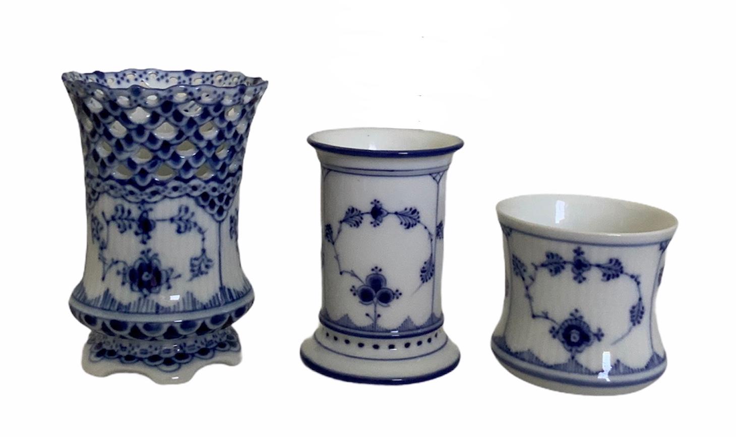 This is a set of three Royal Copenhagen hand painted fluted porcelain cigars or cigarettes cups/small vases. All of them are navy blue and white with a chinoiserie like pattern design of a creeper of flowers in the center. The largest one has a