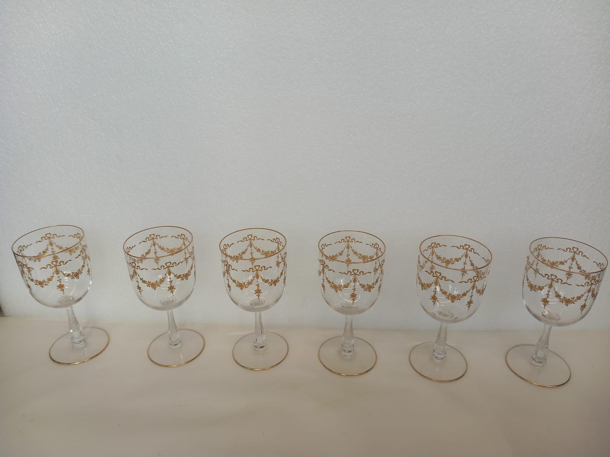 A fantastic set of Saint Louis crystal glasses dating from the late nineteenth century. Each piece is hand decorated with gold swags of flowers and bows, the stems have a slight cut design to make the holding of the glass comfortable. 
The beautiful