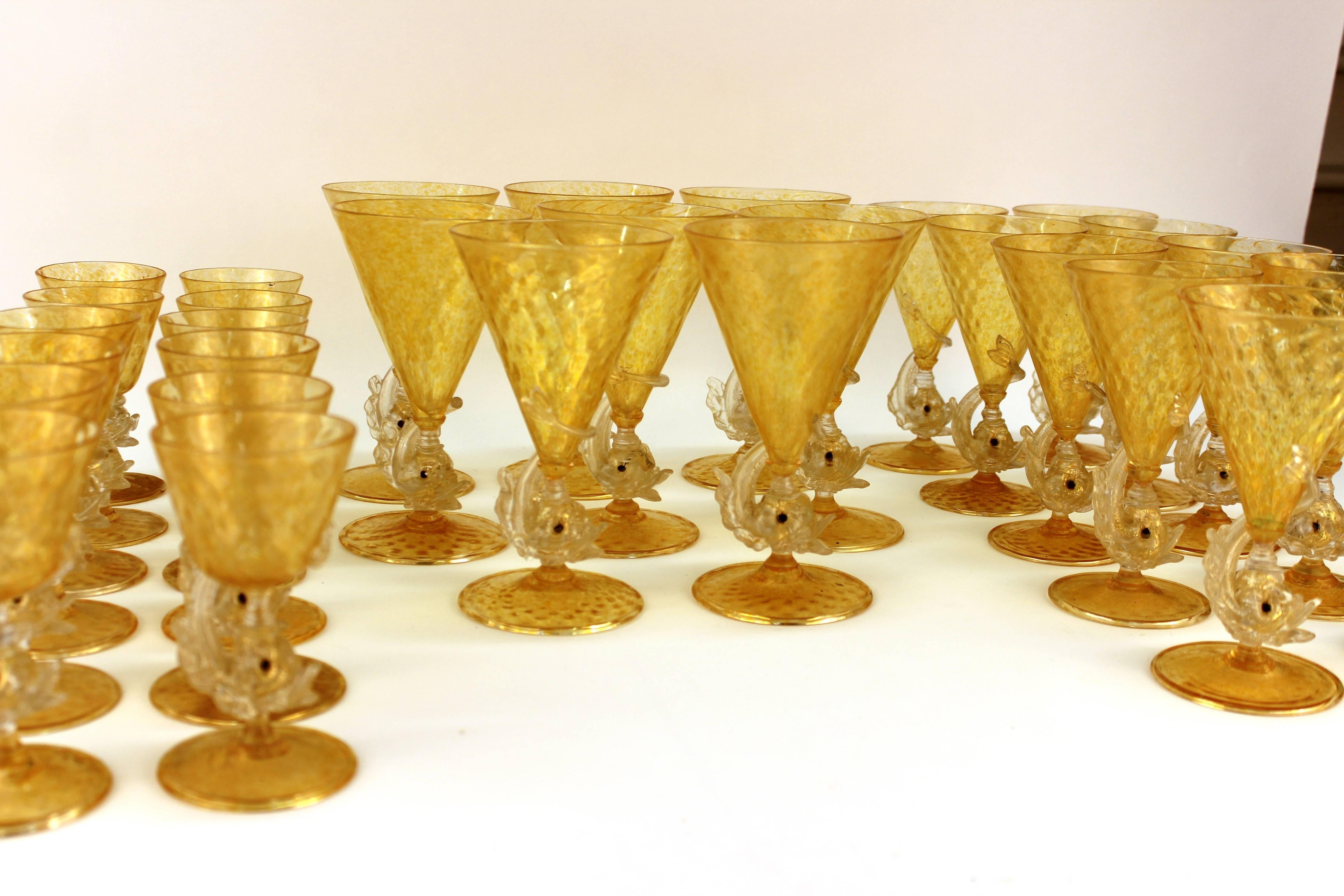 Salviati glassware set including ten wine glasses, 12 liquor glasses and eight water glasses. Each piece is crafted from yellow specked Murano glass. Each stem features stylized fish curving from the base to the bottom of the cup. Some chips and