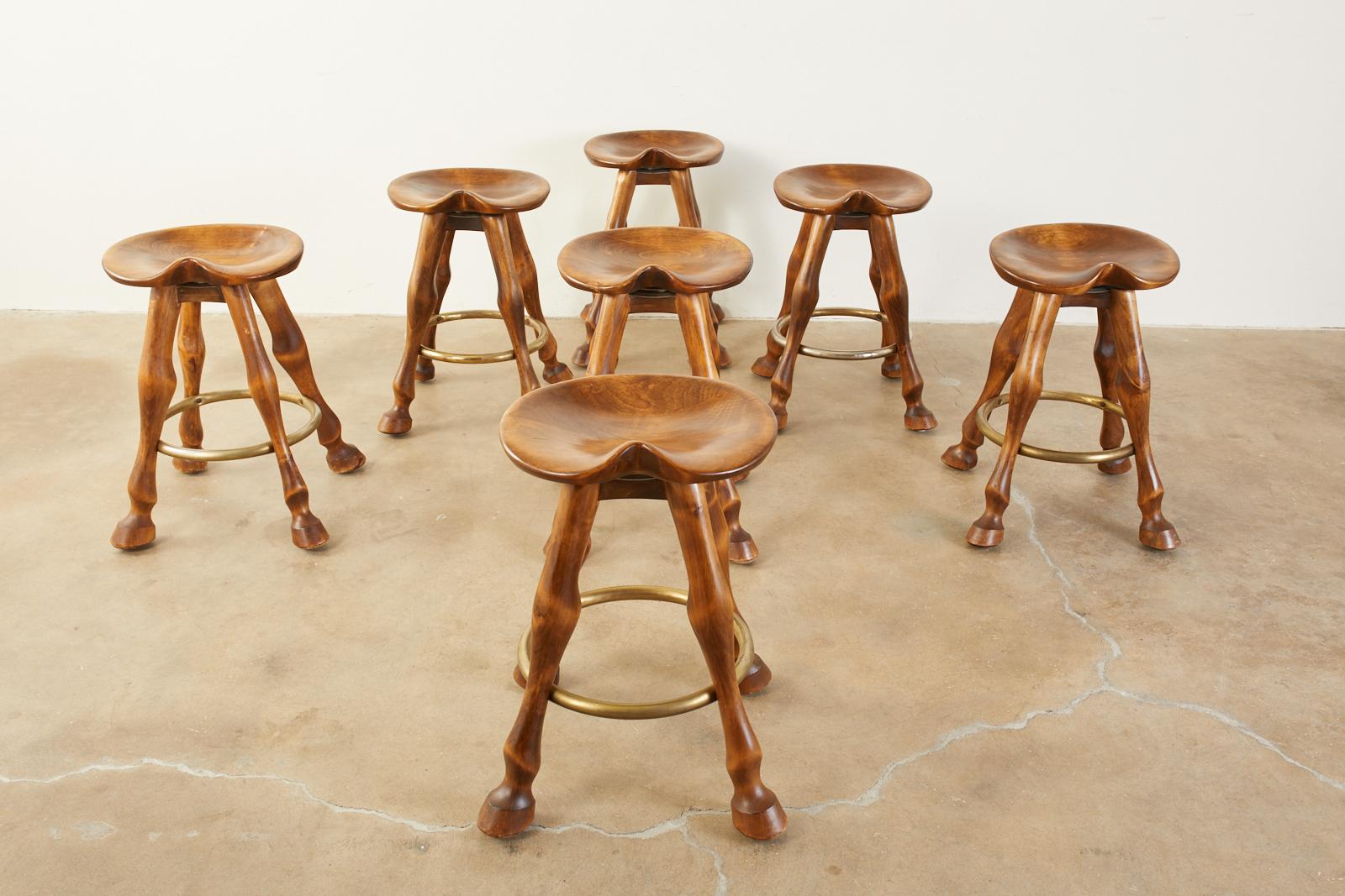 Rustic set of seven carved barstools with saddle shaped seats. The stools are counter height (24.5 inches) tall and feature horse legs ending with hoof feet. Made in the Western Americana style showcasing the rich oakwood grains and rich finish. The