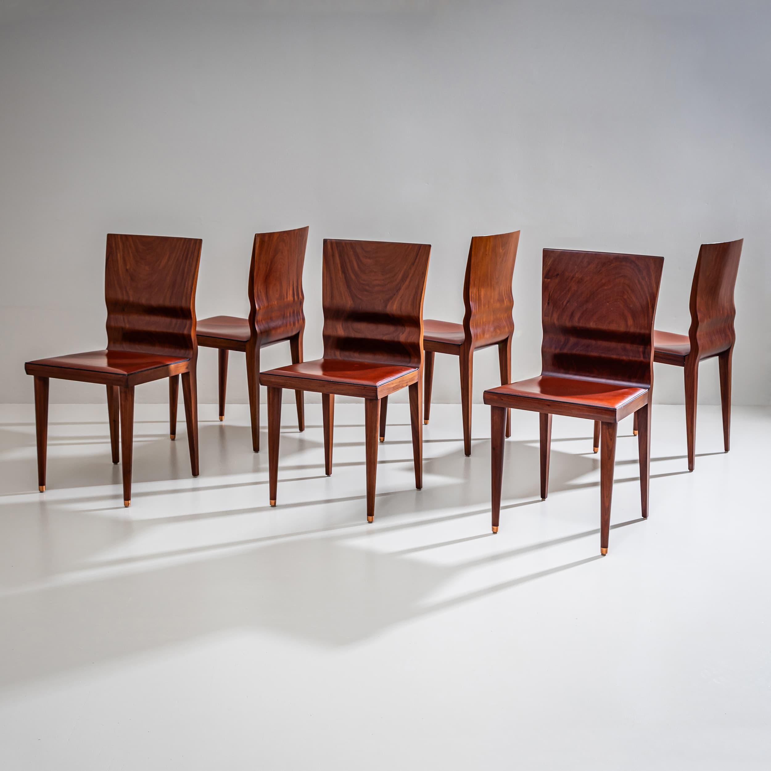 Eleganti sedie realizzate in noce lucidato con uno schienale ergonomico a forma di onda scultorea. Le gambe affusolate sono rifinite nella parte anteriore con raffinati accenti in ottone. I sedili sono rivestiti in pelle marrone rossastra con