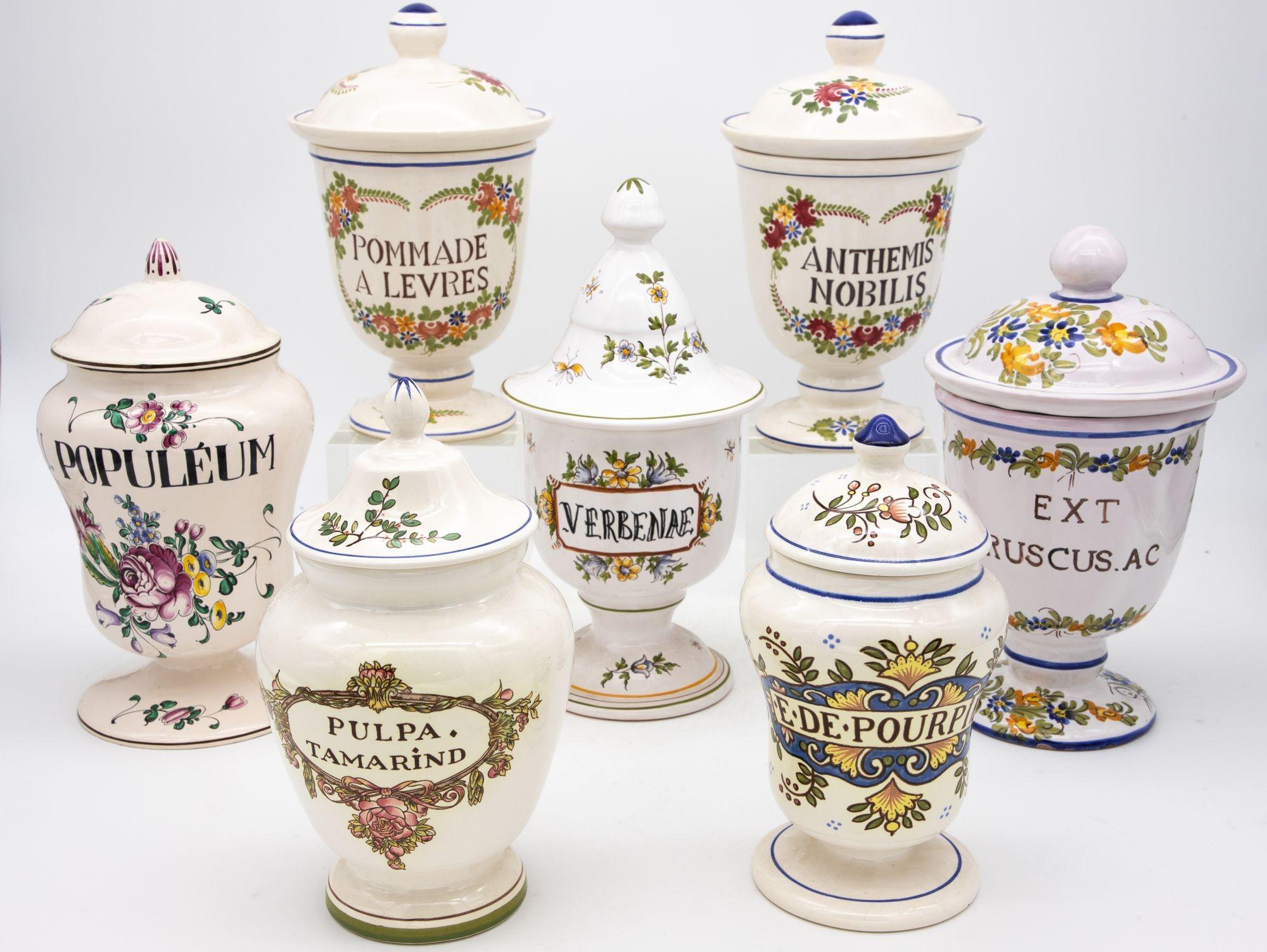 A collection of seven apothecary jars in a Provence style. Each painted apothecary or pharmacy jar has a name and unique design painted on it. The collection is early 20th century and each has its lid. The smallest measures 4.5