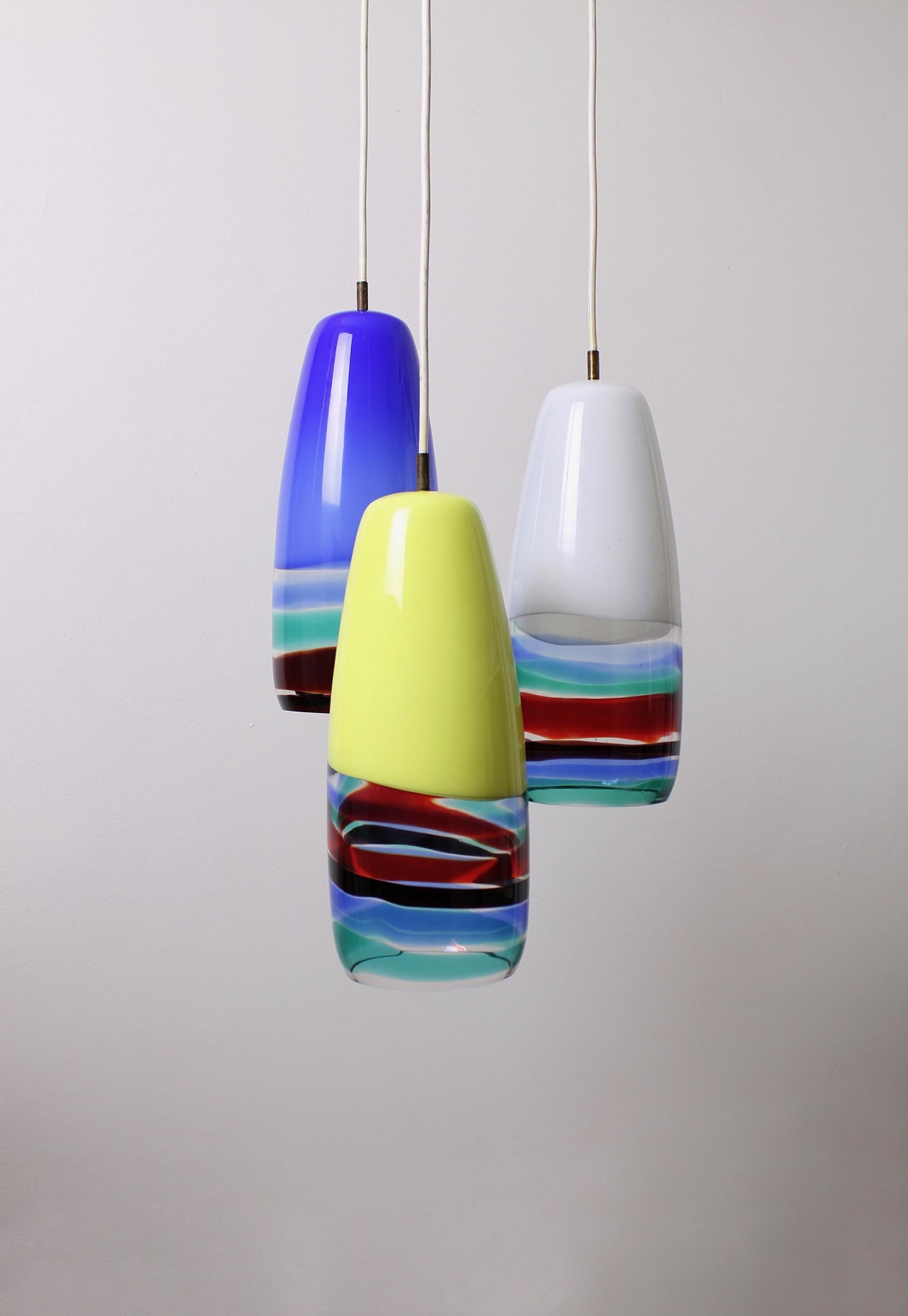 Iconic set of three Sigaro pendant lamps, designed during the collaboration between Massimo Vignelli and Venini in 1956. The lamps are made of lattimo glass with multicolored bands on the bottom of the lamp. Vignelli designed the lamps to be