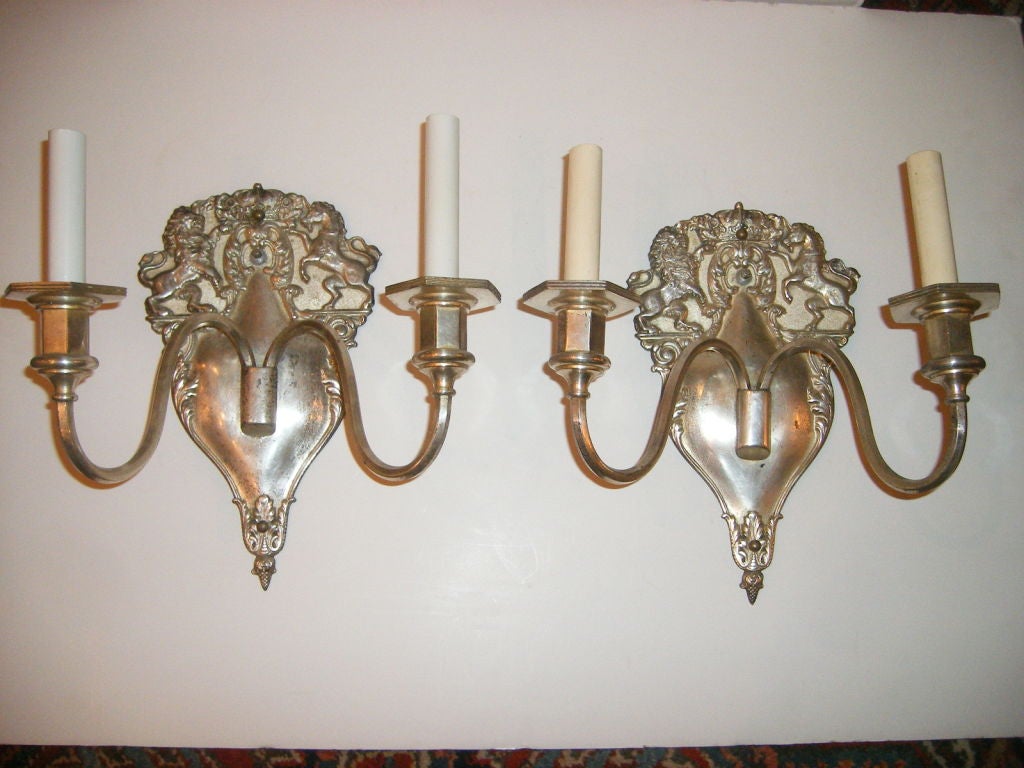 Set of 8 English, circa 1920s silver plated double light sconces with British coat of arms on shield shaped backplate with unicorn and lion flanking a royal crown. Sold in pairs.

Measurements:
Height: 12.5