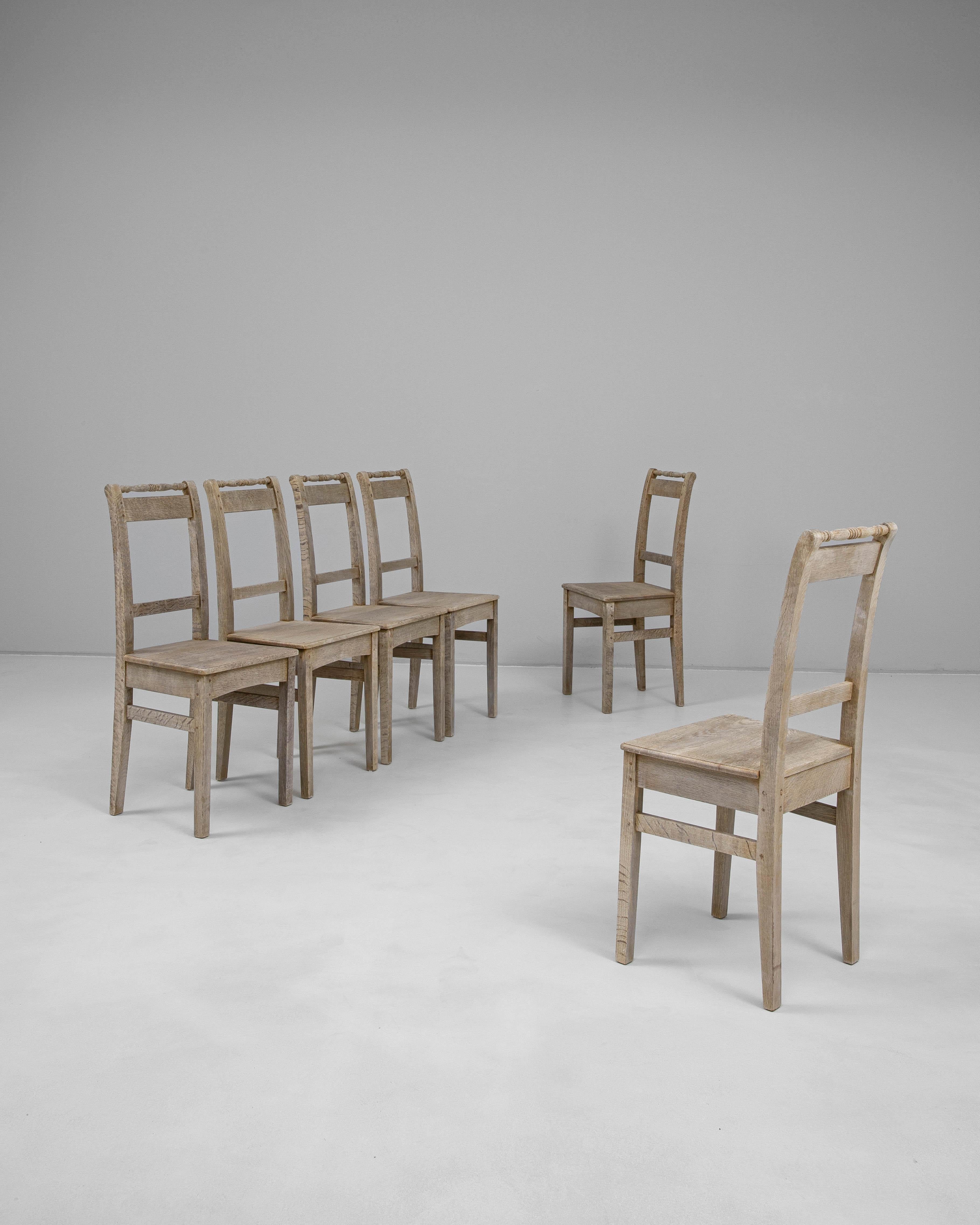Set di sei sedie da pranzo in rovere francese del 1900, realizzate con linee semplici e senza tempo e con una patina rustica che ne testimonia l'età e l'utilizzo. Ogni sedia è caratterizzata da un design con schienale a scaletta, una barra superiore