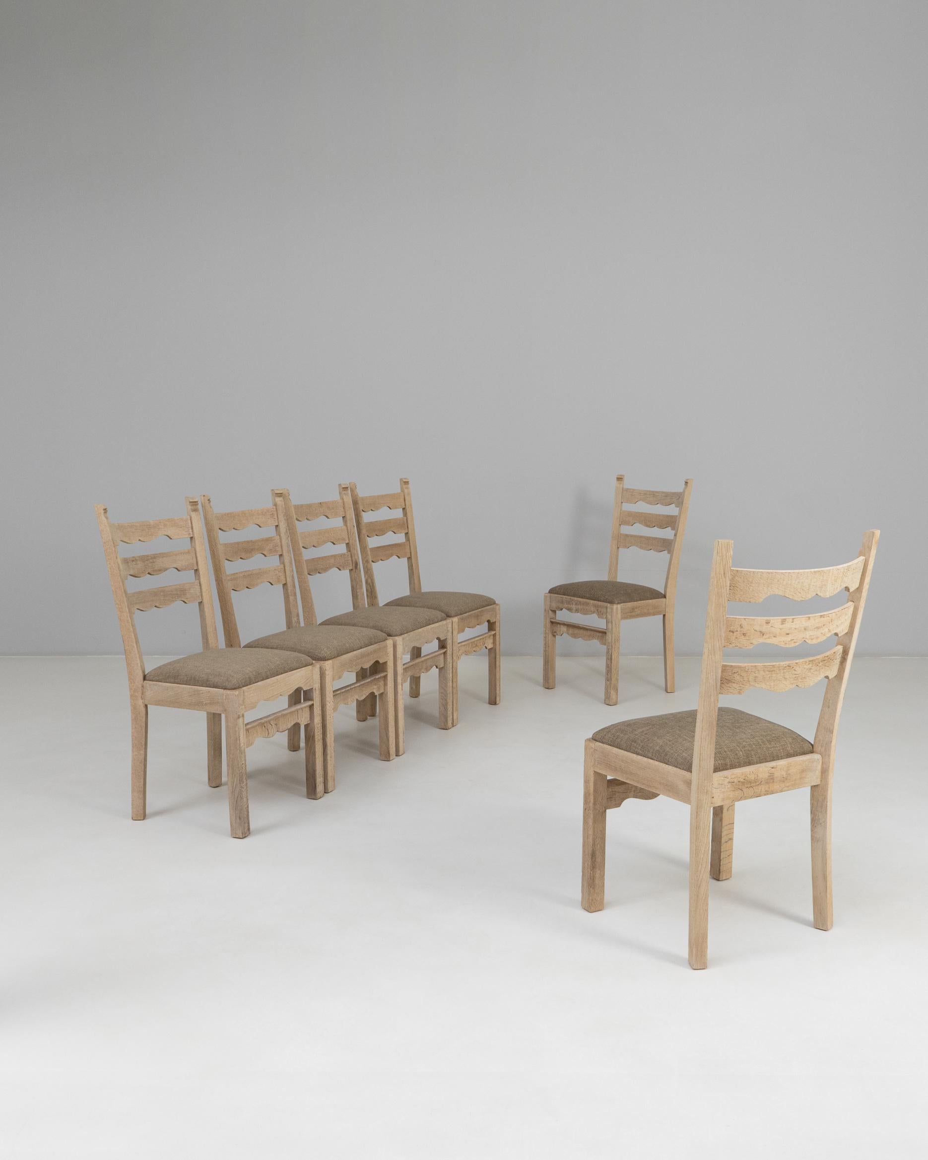 This set of six 1950s French oak dining chairs presents a clean, refined interpretation of classic provincial design. Each chair features a ladder-back silhouette with subtly carved rails, adding gentle visual movement while maintaining an