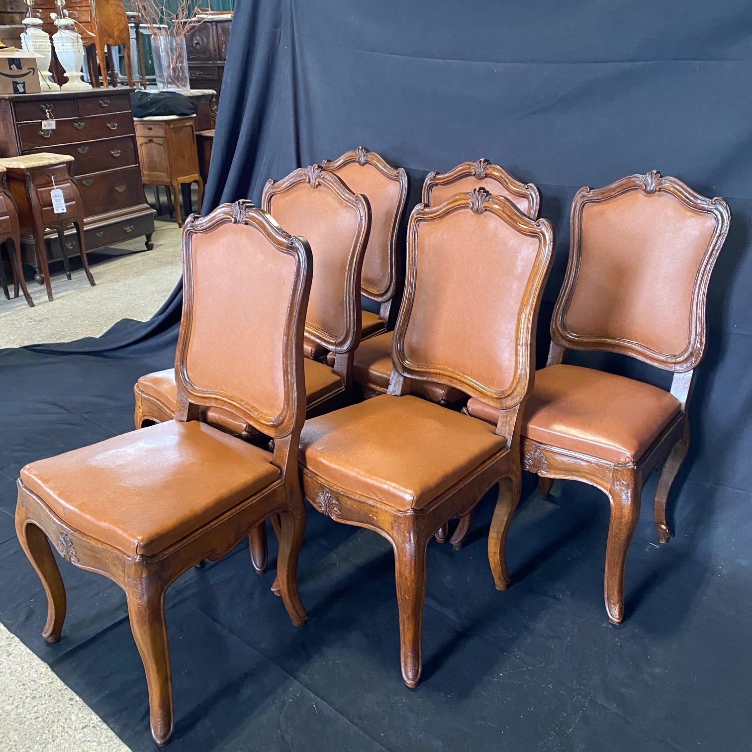 Absolutely stunning set of six early 19th century (or earlier) walnut carved Italian dining or side chairs. Aprons display lovely floret and chairs show peg construction and are solid and comfortable. Seats are aged worn faux leather that looks real