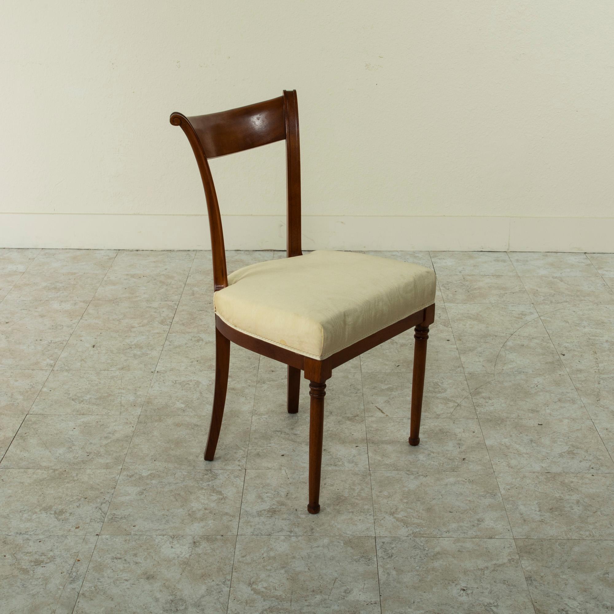 This set of six French Directoire style dining chairs from the mid-20th century are constructed of solid walnut. They feature scrolled seat backs and turned front legs. The square back legs curve gently 