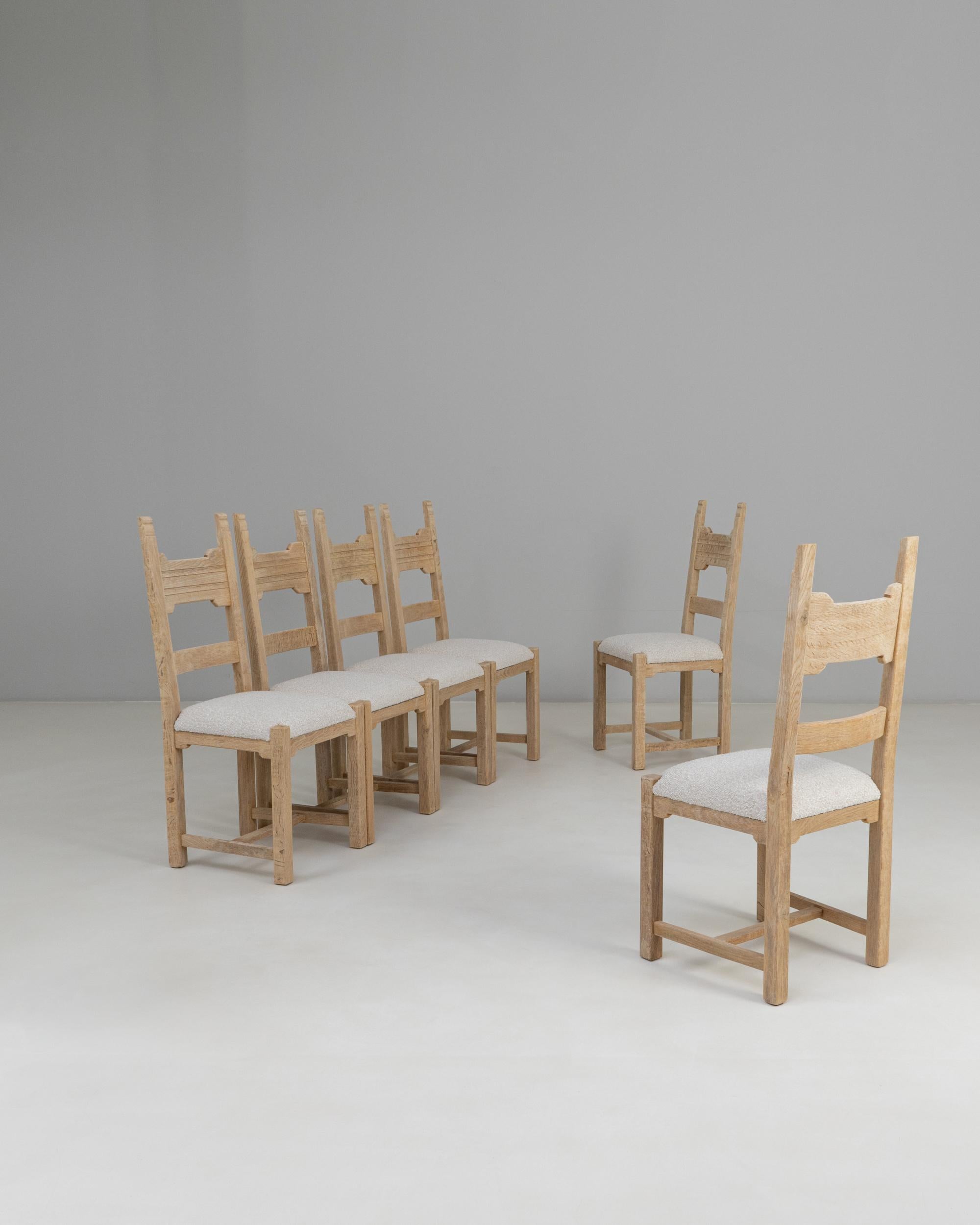 This set of six 20th century French oak dining chairs offers a refined provincial aesthetic with clean lines and thoughtful craftsmanship. Each chair features a ladder-back design characterized by gently carved rails that introduce subtle texture