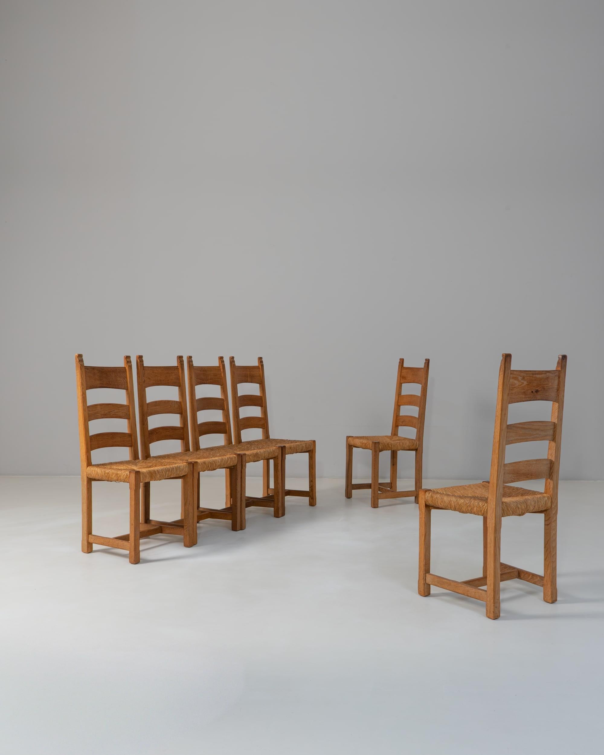 Questo set di sei sedie da pranzo con schienale a scaletta in quercia della provincia francese del XX secolo riflette l'onesta maestria artigianale e la sobria eleganza tipiche del design rurale francese. Ogni sedia è caratterizzata da una