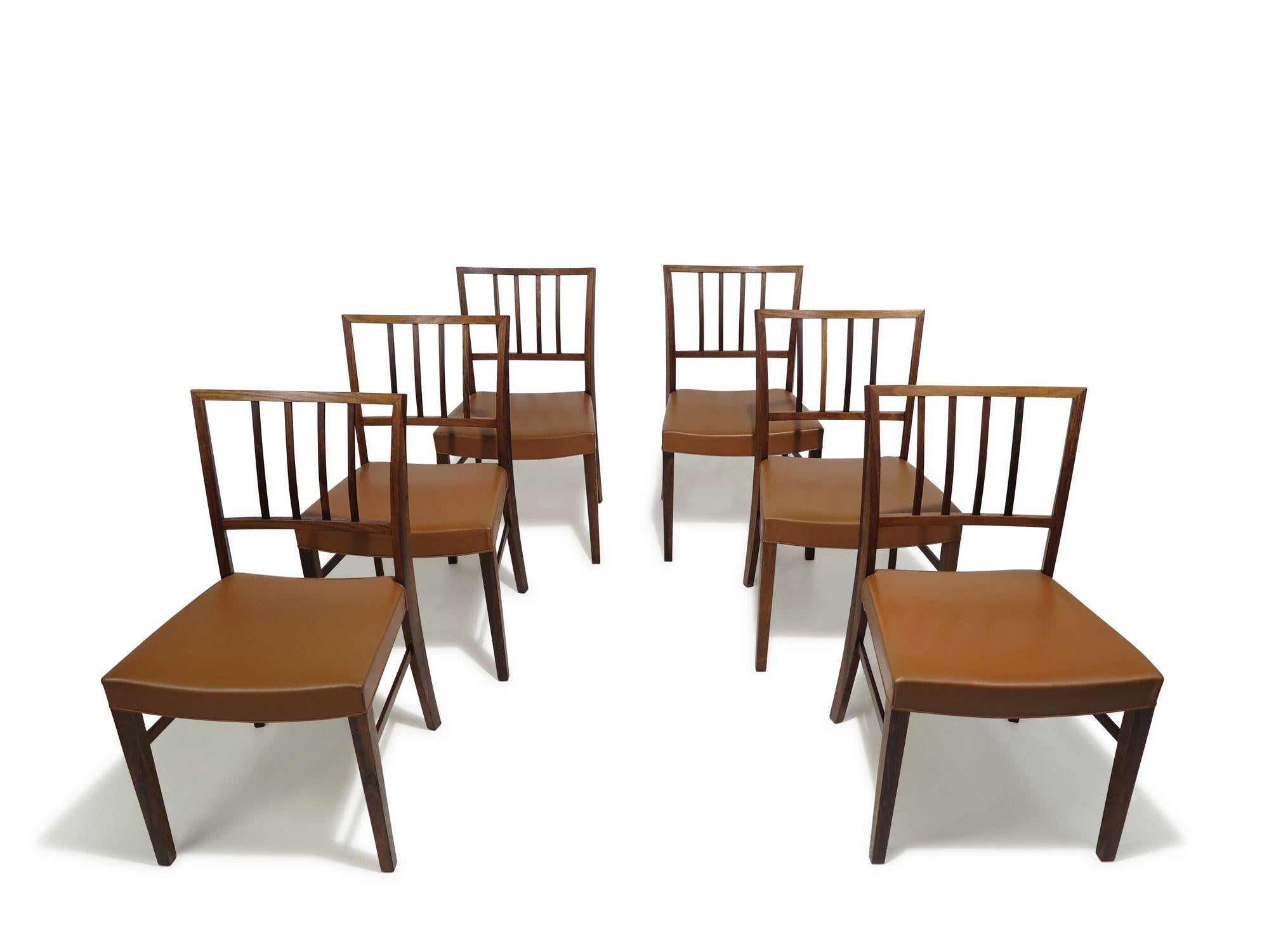 Classic set of six handcrafted rosewood dining chairs in the manner of renowned Danish architect Jacob Kjaer and Ole Wanscher. The chairs feature slightly curved backrests with minimal vertical slatted backs, upholstered in the original saddle