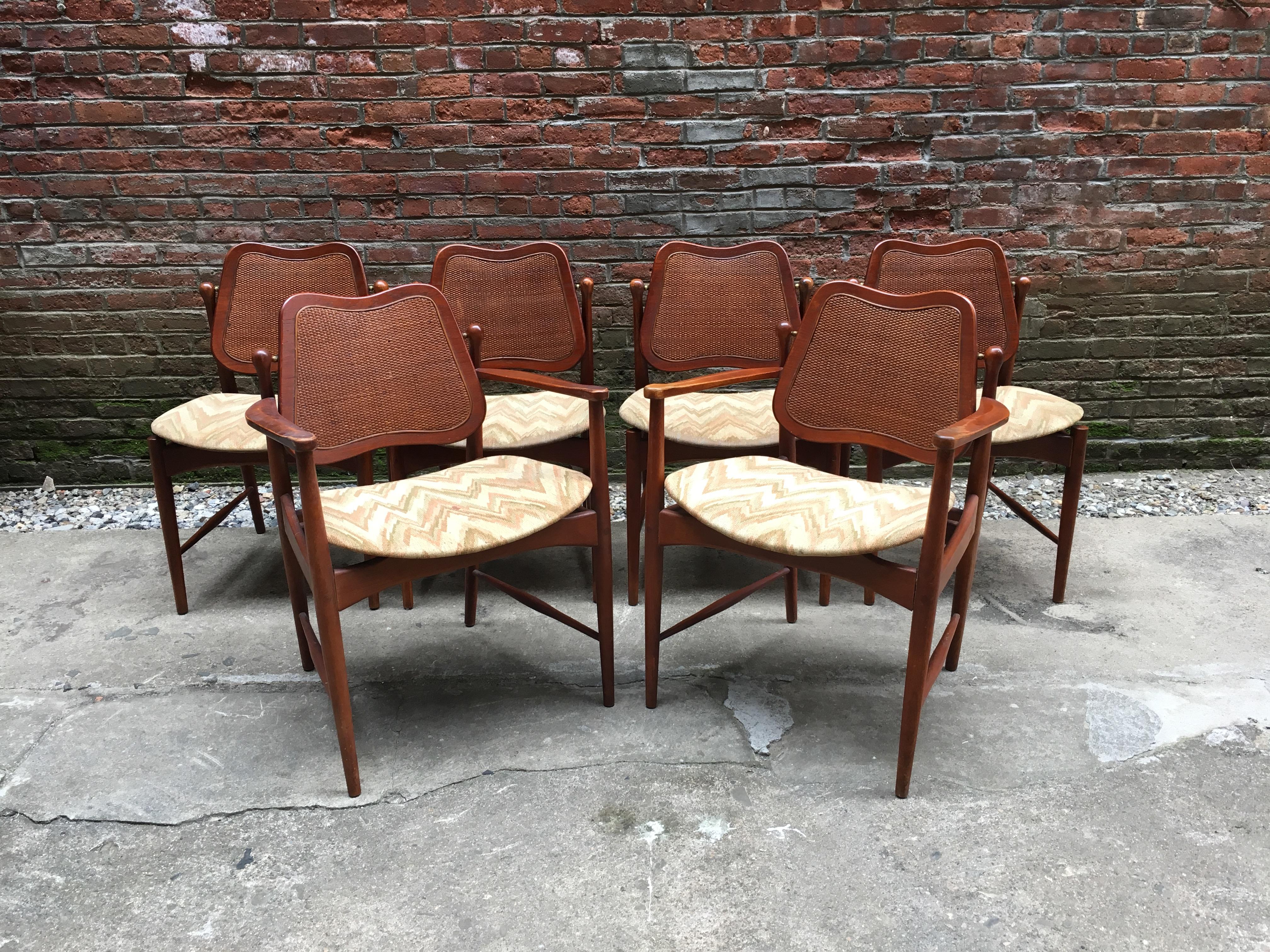 Early and good set of six Danish modern Arne Vodder designed teak and cane back chairs. These beautiful chairs feature solid teak construction, inset caned backs, and brass fittings so the back of the seat tilts when you move for constant back
