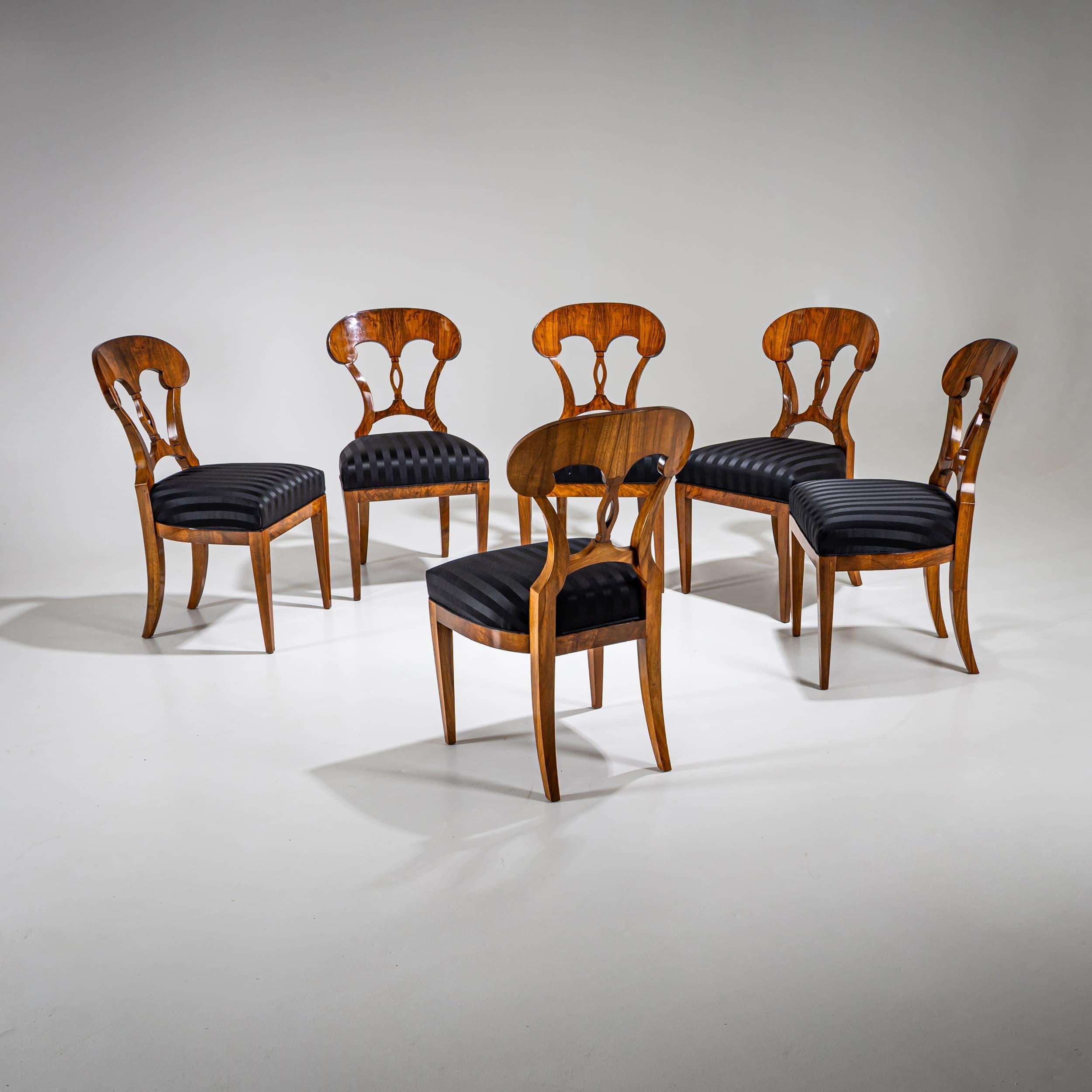 Set of six Biedermeier chairs in walnut. The finely crafted backrests feature an openwork central splat and terminate in a distinctive shovel-shaped crest. The frames are veneered in walnut and hand-polished. Seats have been newly upholstered in a