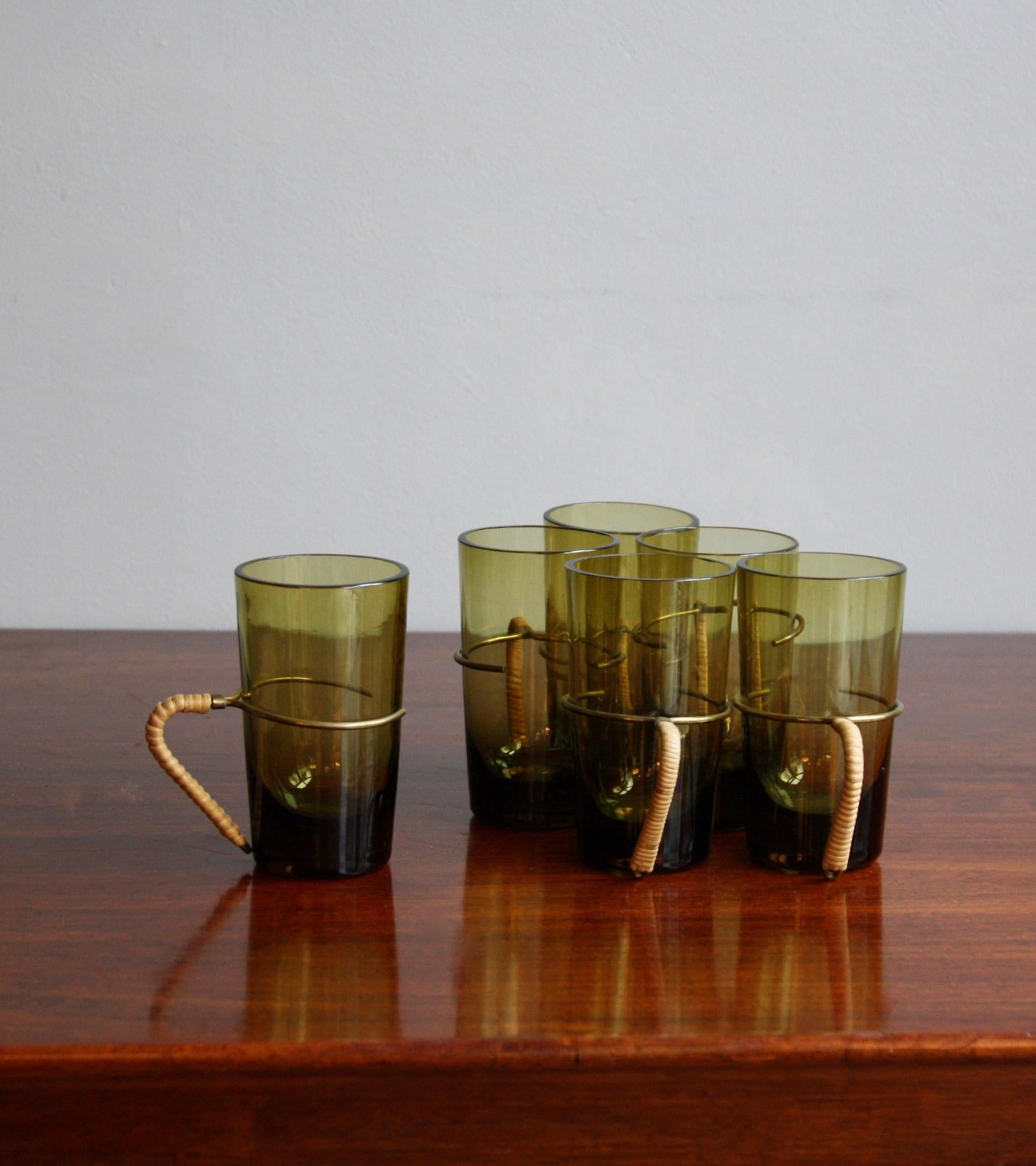 A set of six glasses with wicker bound brass handles designed by Carl Auböck II, Vienna, circa 1950.
The transparent antique-bottle-green coloured glasses are thick bottomed and thin at the rim. The varying gauge of the glass means the item is very