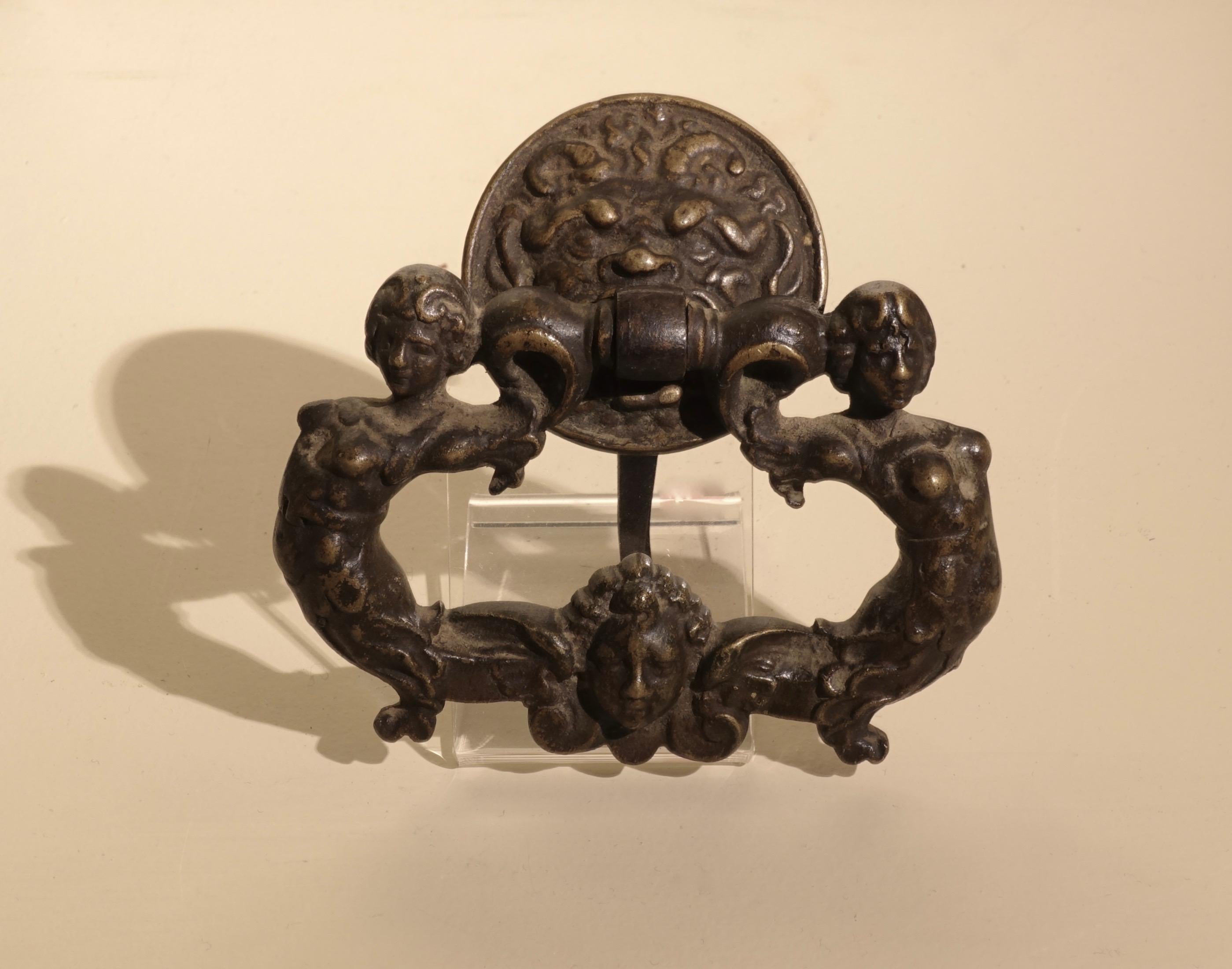 Set of six chiseled bronze handles decorated with mermaids and mascarons
Central Italy, 16th century
Bronze
Measures: 11.4 x 12 x 8cm

Finely worked bronze drawer sockets representing two confronting sirens surrounding a cherub head and a