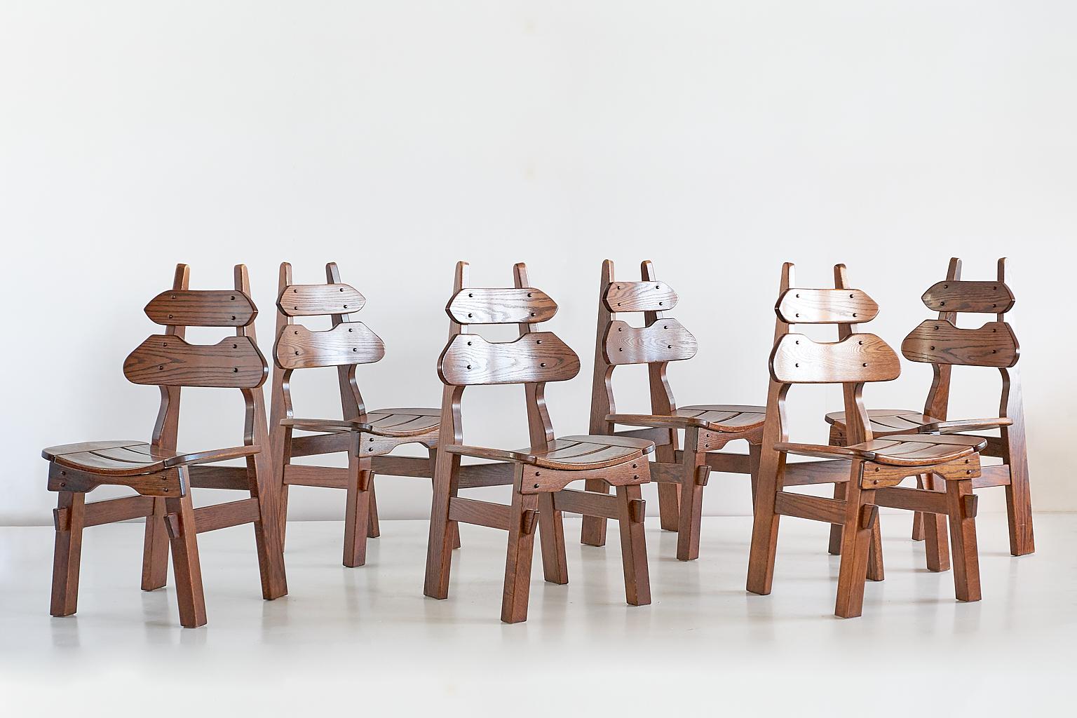 This impressive set of six Brutalist dining chairs was produced in Spain in the 1970s. The well constructed chairs are made of solid oak, with the striking grain of the wood highlighted by the dark stain finish. The slightly curved backrest and seat