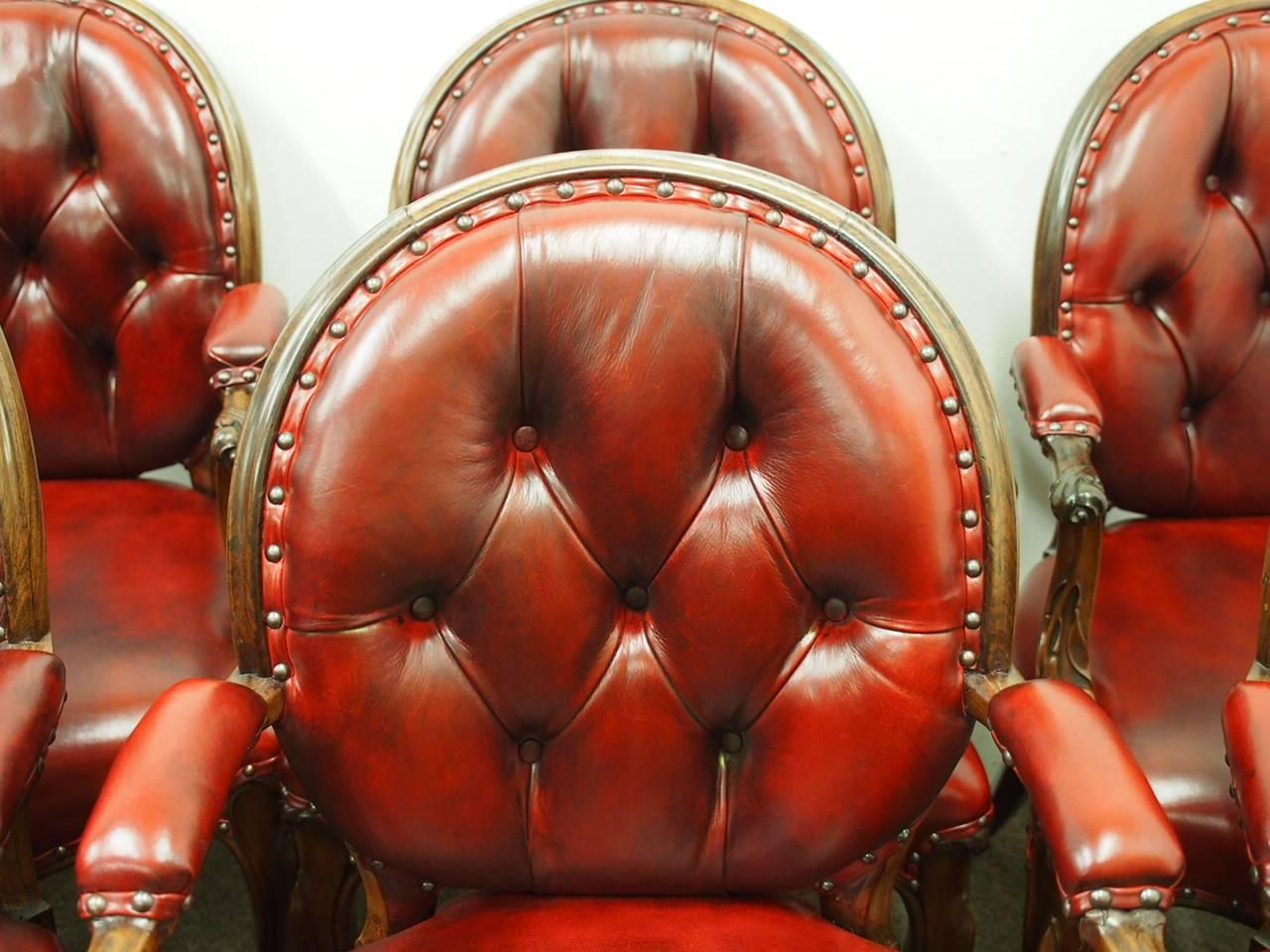 Rare set of six carved rosewood armchairs, circa 1860. With oval carved backs framed in rosewood and deep buttoned red leather (with brass studding). There is further leather padding to sections of the arms, and foliate carving continues from the