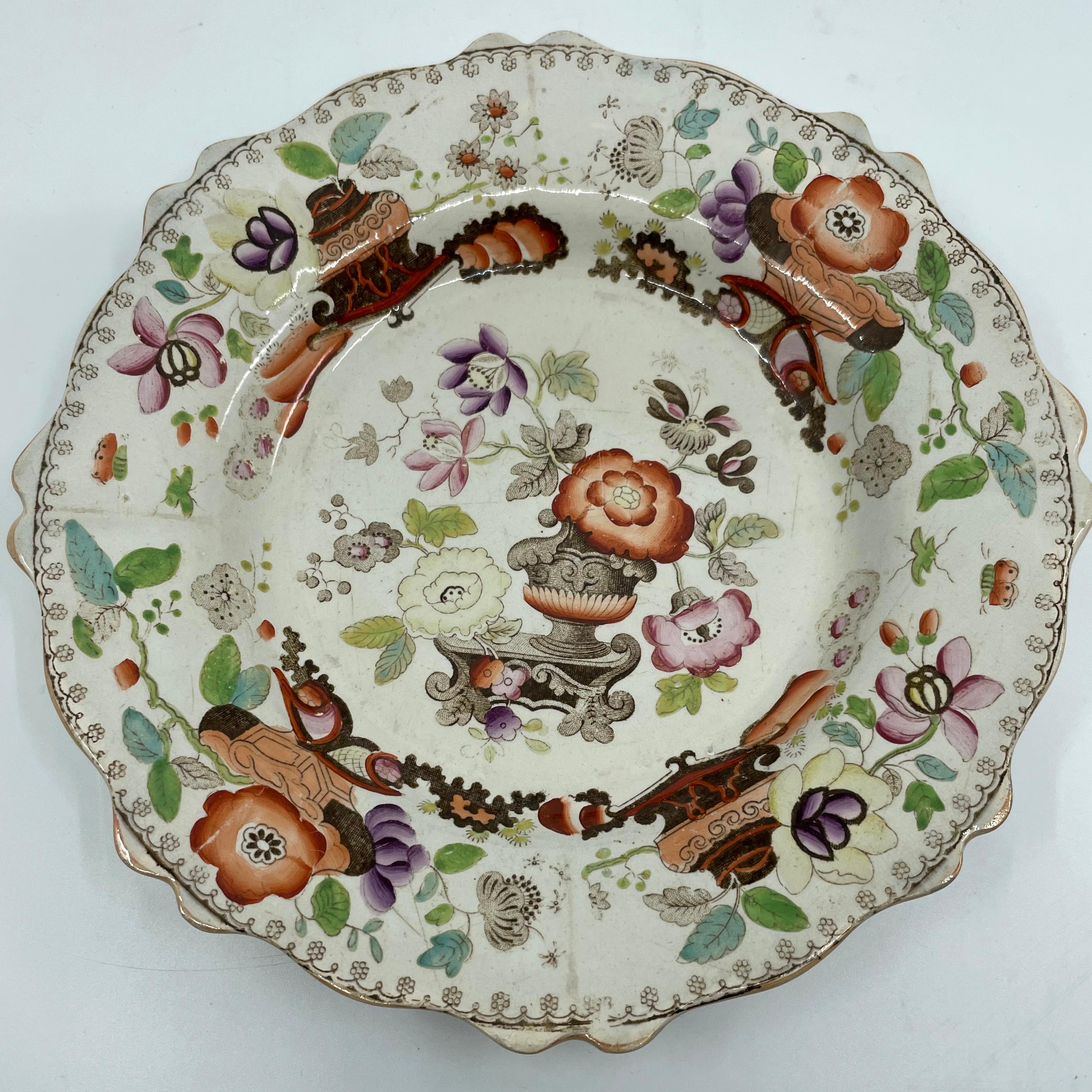 Set of six Chinoiserie plates. Six ironstone plates in an autumnal Imari pattern in oranges, browns, puce and greens with peony flowers in urns surrounded by rocks, further blooms and butterflies with shaped and lobed borders with orange lustre