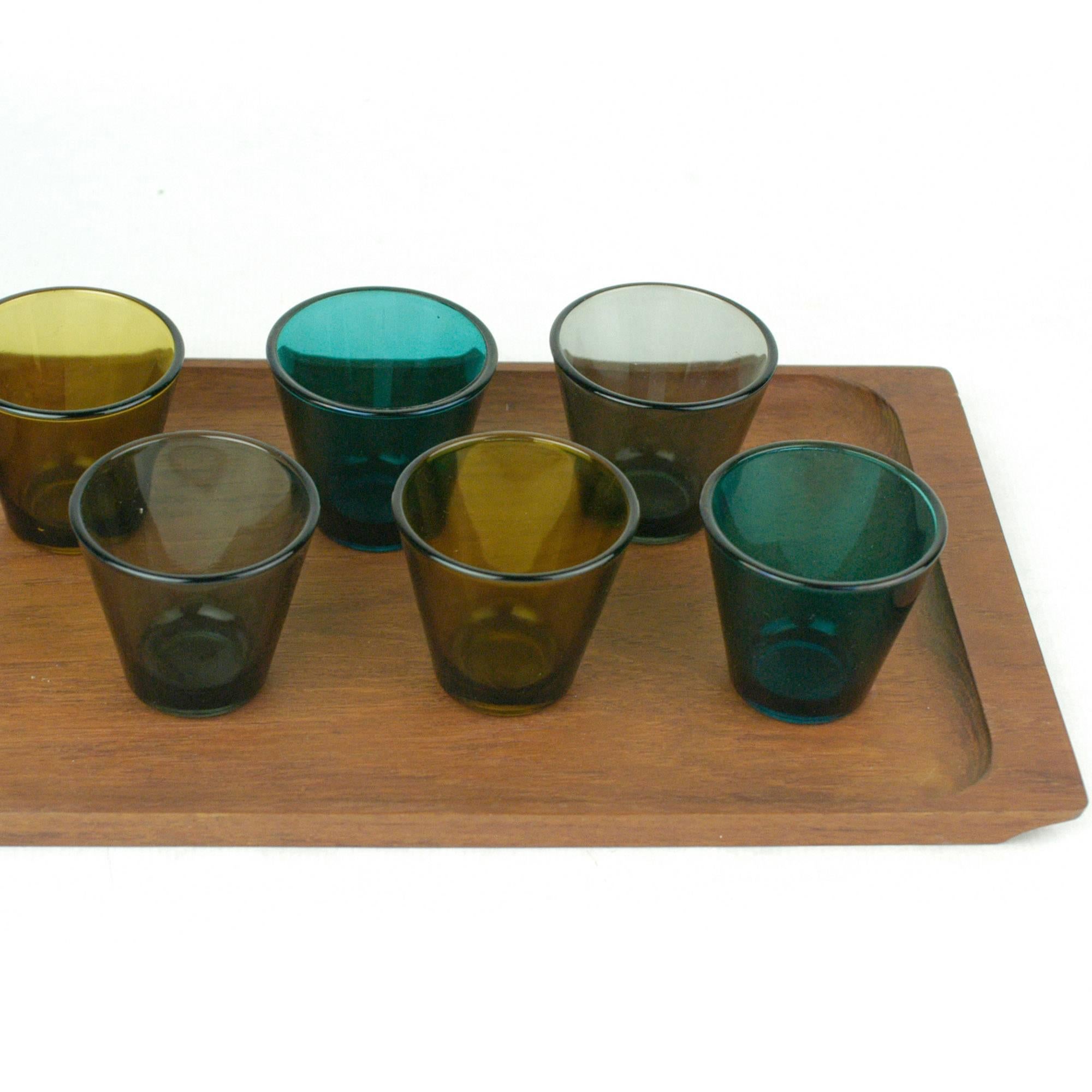 Charming set of iconic Scandinavian Modern liquor glasses in different colors with matching teak tray. All glasses are in perfect condition. They are designed by the finish Designer Kaj Franck and are part of the iconic model Kartio glass series