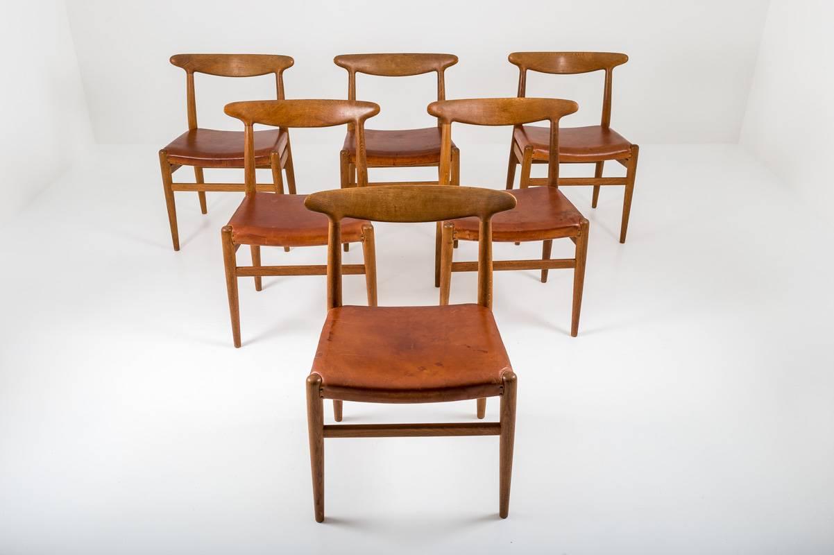 A set of six stunning dining chairs model W2 by Hans J. Wegner, Denmark. The chairs are made of solid oak and have their original leather seats. The chairs show an impressive patina on the leather and frames and are carefully restored to keep them