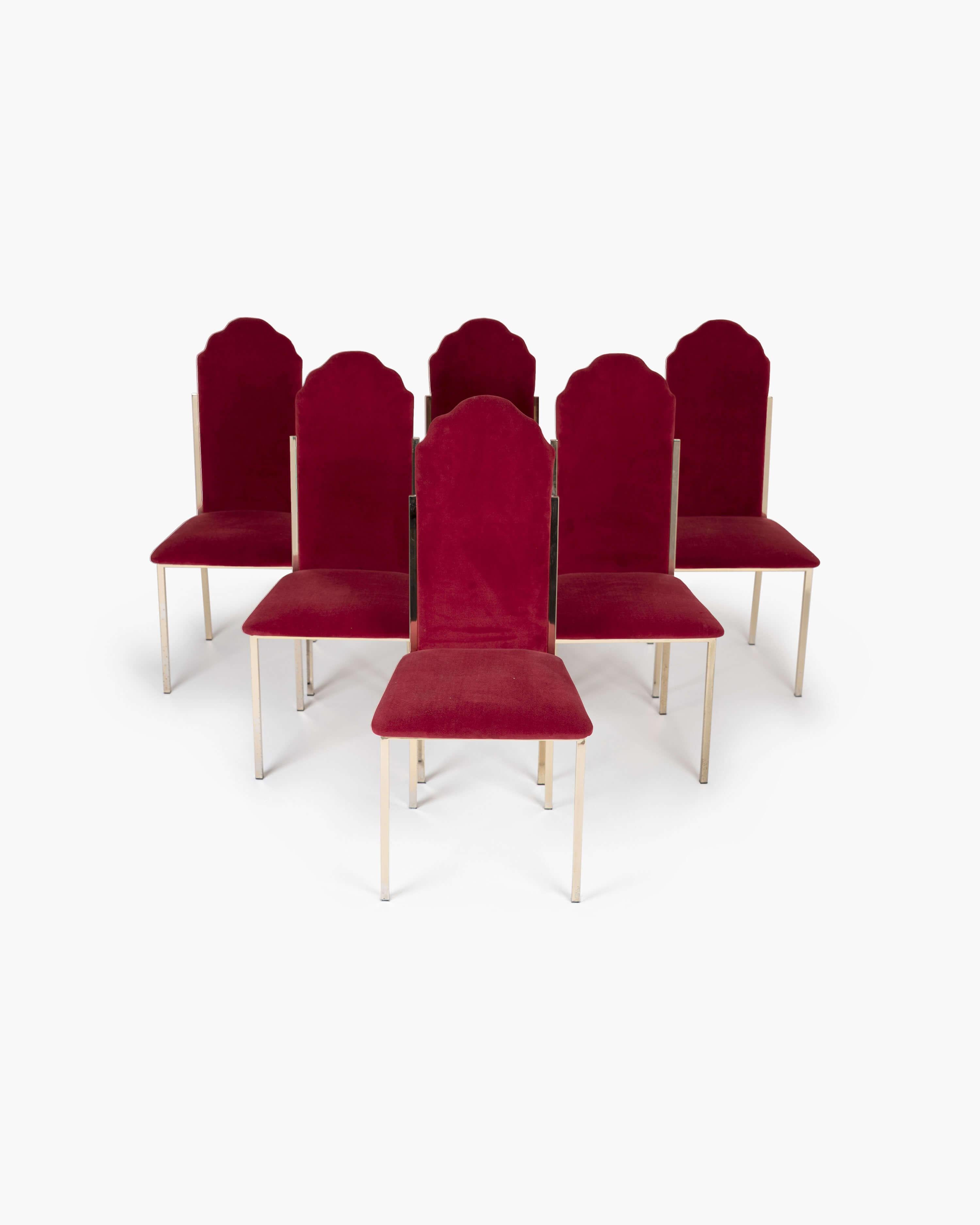 Designed by French cinema icon Alain Delon for the Paris-based interior decoration house Maison Jansen, this set of six Hollywood Regency dining chairs feature a scalloped high-back and slender brass frame with red velvet upholstery.