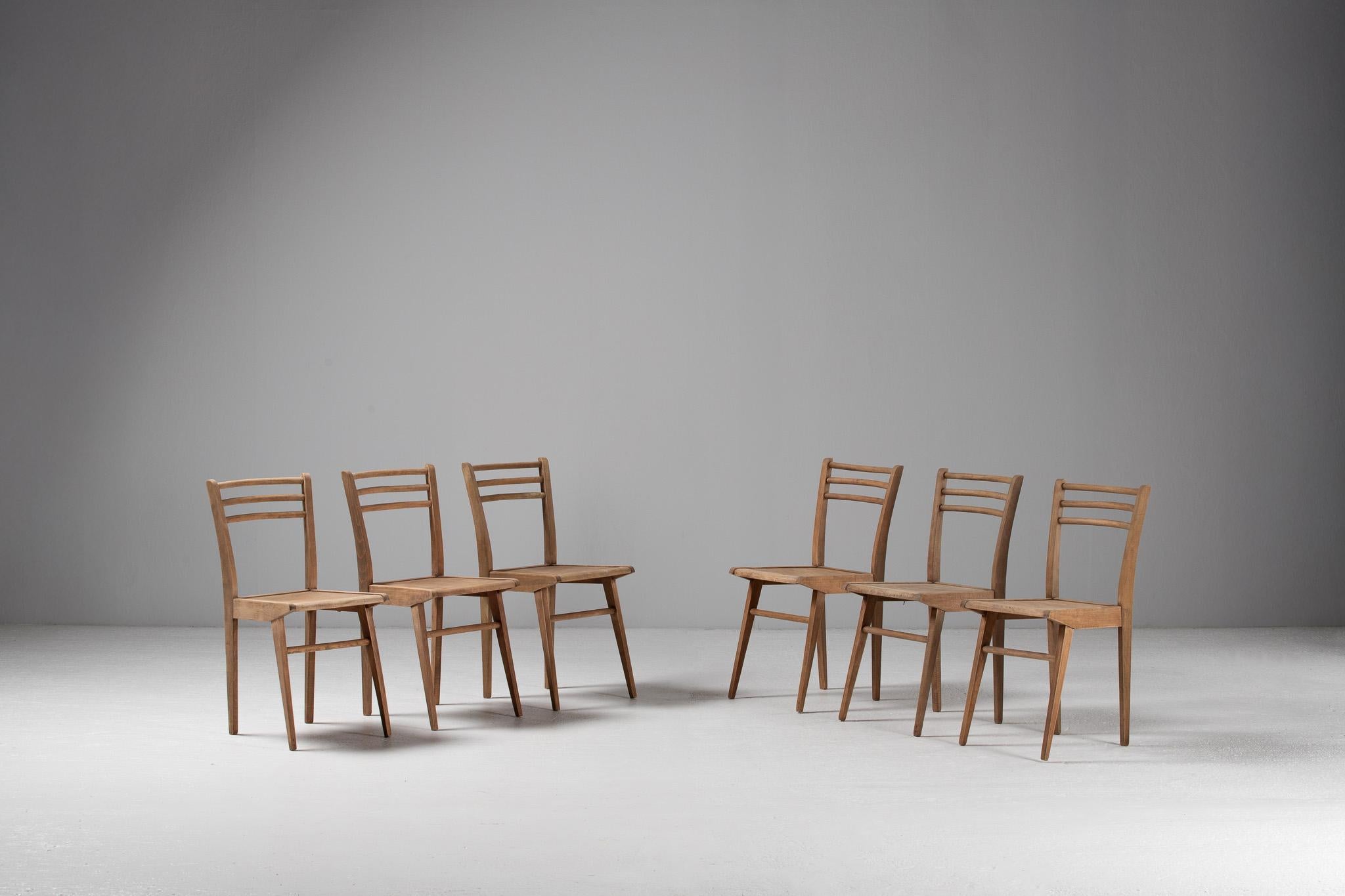 Sobrio y poético, este conjunto de seis sillas de comedor francesas encarna la tranquila claridad del diseño vernáculo de mediados de siglo. Sus siluetas están definidas por una suave conicidad y raíles traseros de arco contenido que flotan como