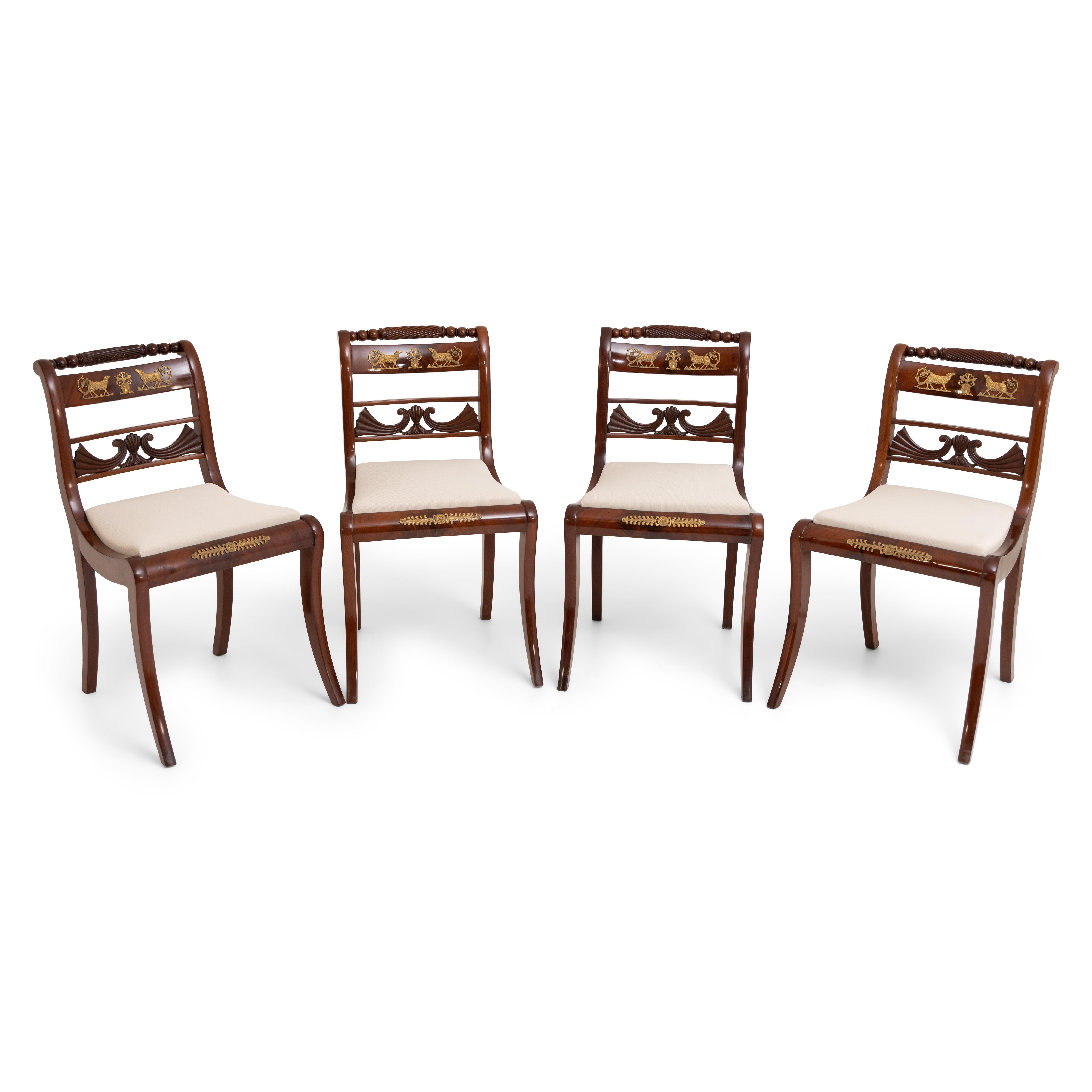 Set of six chairs, consisting of four chairs and two armchairs out of mahogany, circa 1830. The chairs stand on sabre legs and are decorated with bronze fittings in the shape of lambs and leaves. The backrests show a pierced carved center strut in