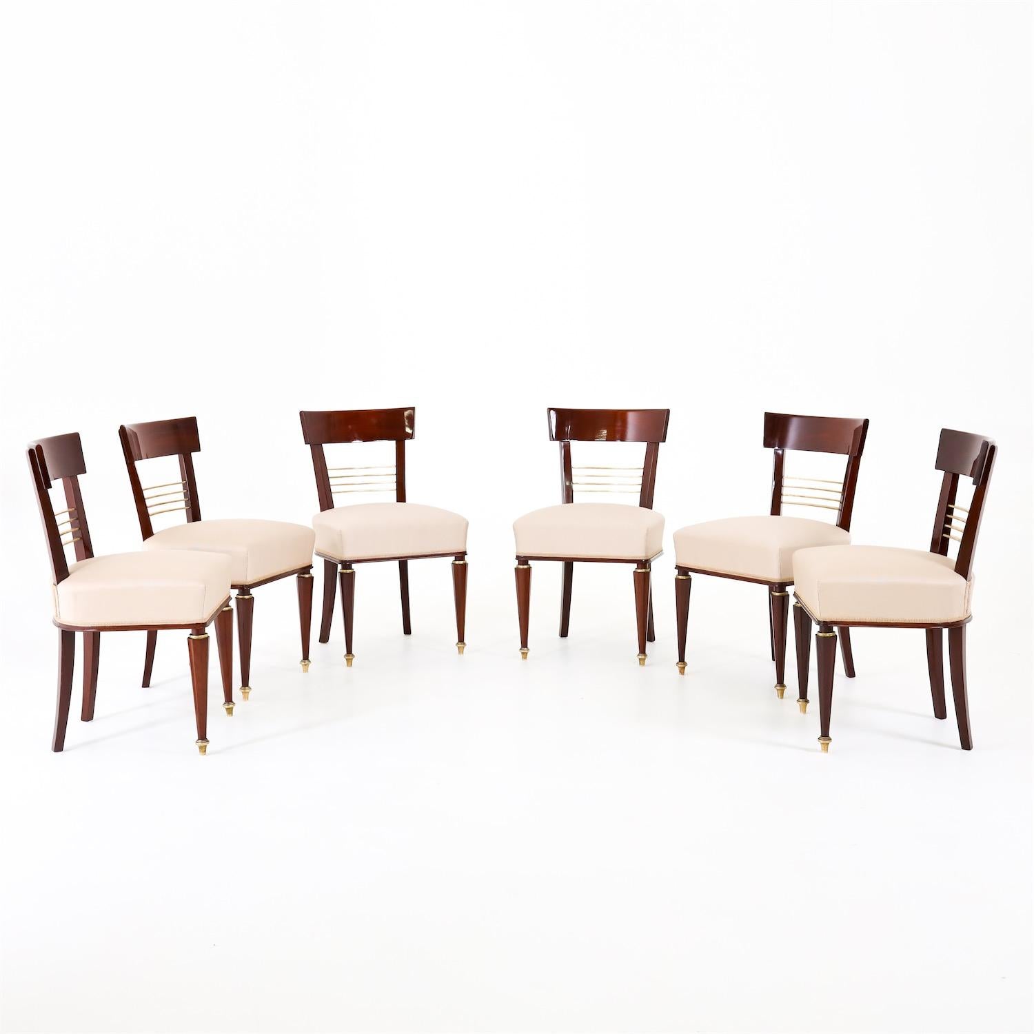 Set of six dining chairs in mahogany, with brass bracing in the backrest, standing on octagonal pointed legs with brass sabots in the front, and slightly flared legs in the back. The chairs have been reupholstered in a high-quality beige fabric with