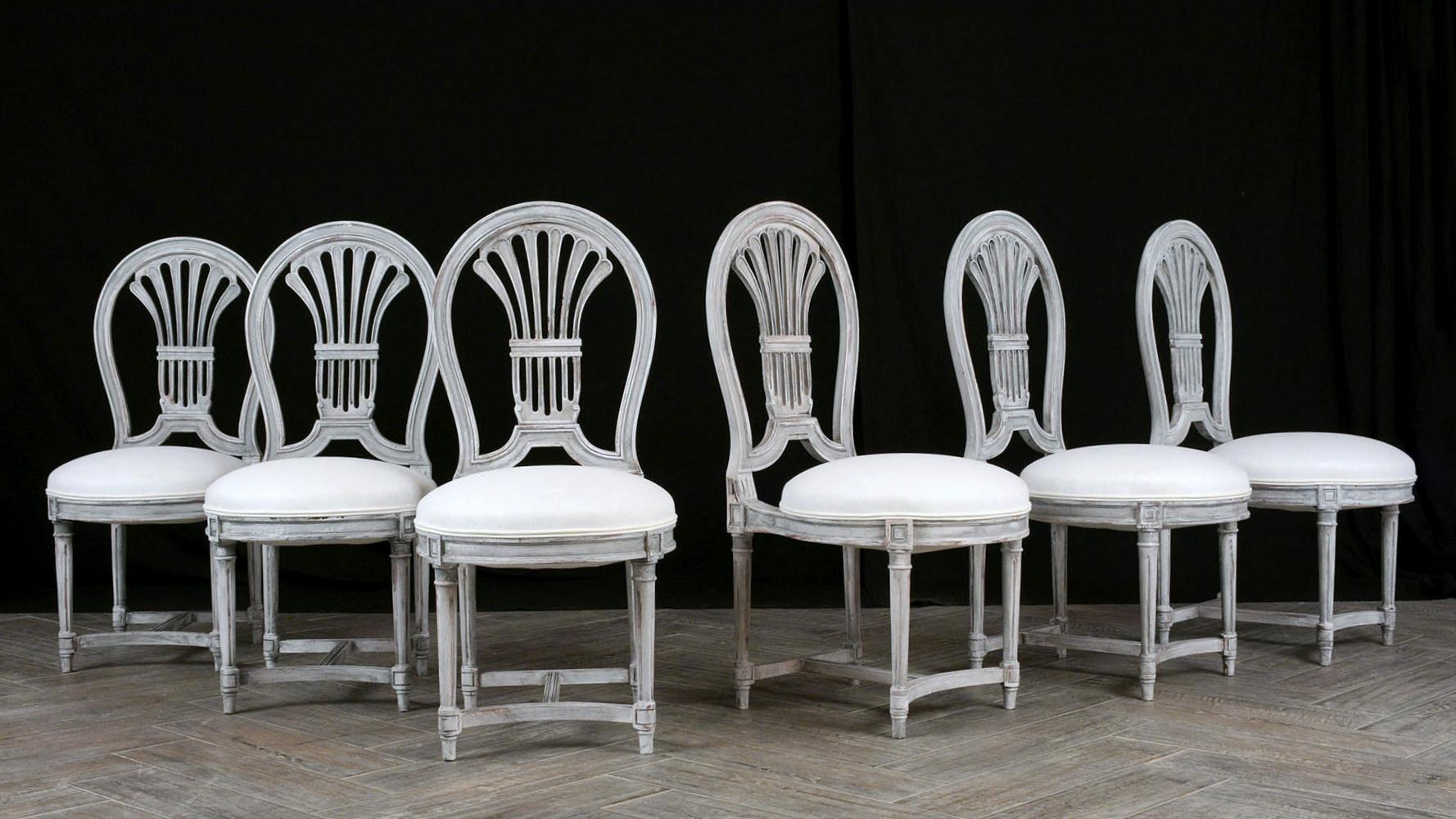 This Set of Six Elegant Dining Chairs made out of mahogany wood with carved back details are in great condition and are newly painted in a beautiful pale gray color with a distressed finish. The seats have been professionally reupholstered in a new
