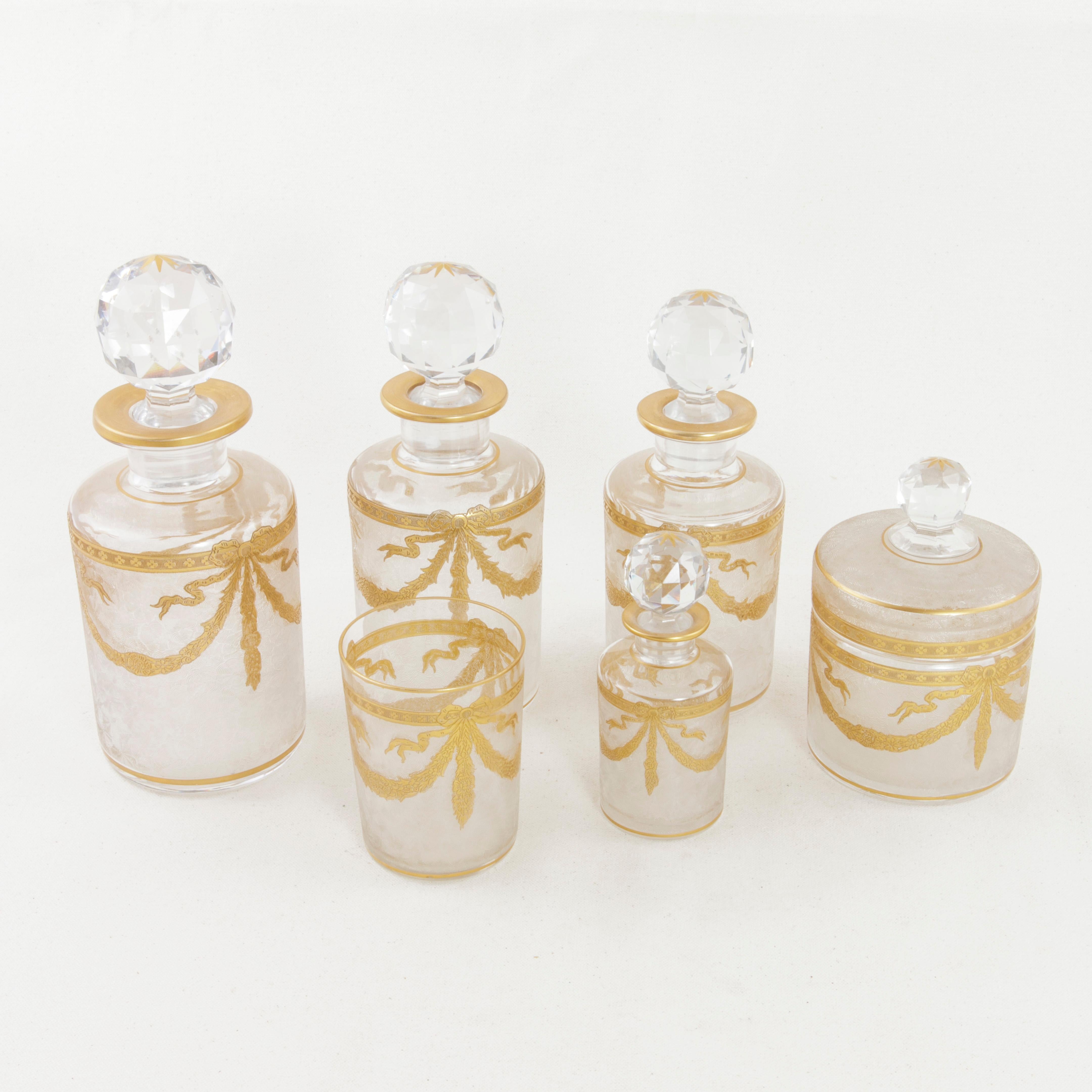 This set of six early 20th century French baccarat crystal vanity bottles features Classic Louis XVI style gold detailing. Gold garlands and knotted ribbons surround each bottle, and gold rims encircle the opening for the cut crystal stoppers. This