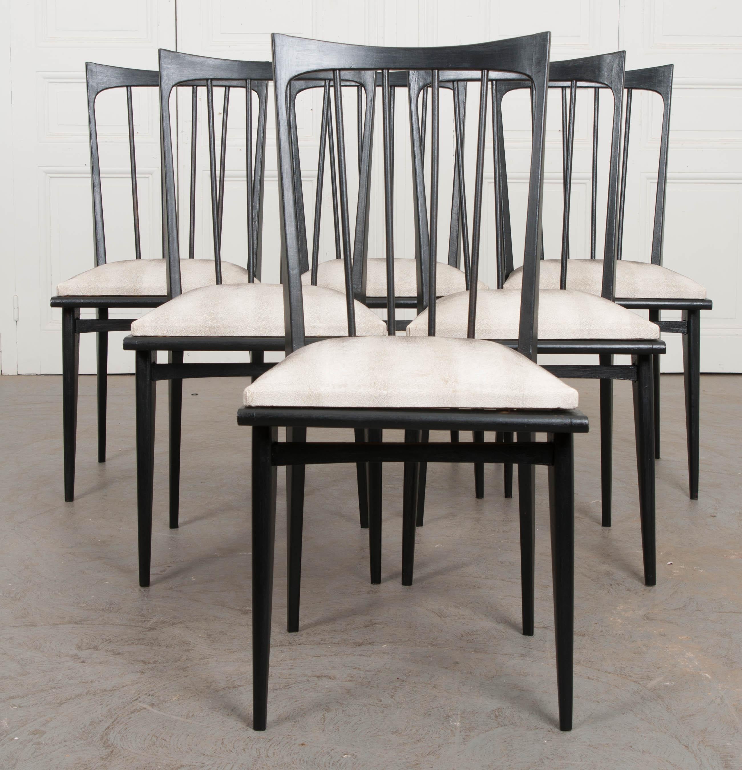 A smart set of dining chairs, recently painted black, from the earlier part of the 20th century, France. The chairs have a funky style, with their backs done in a shaped comb-form and angular seats. The seats are upholstered in an ivory textured
