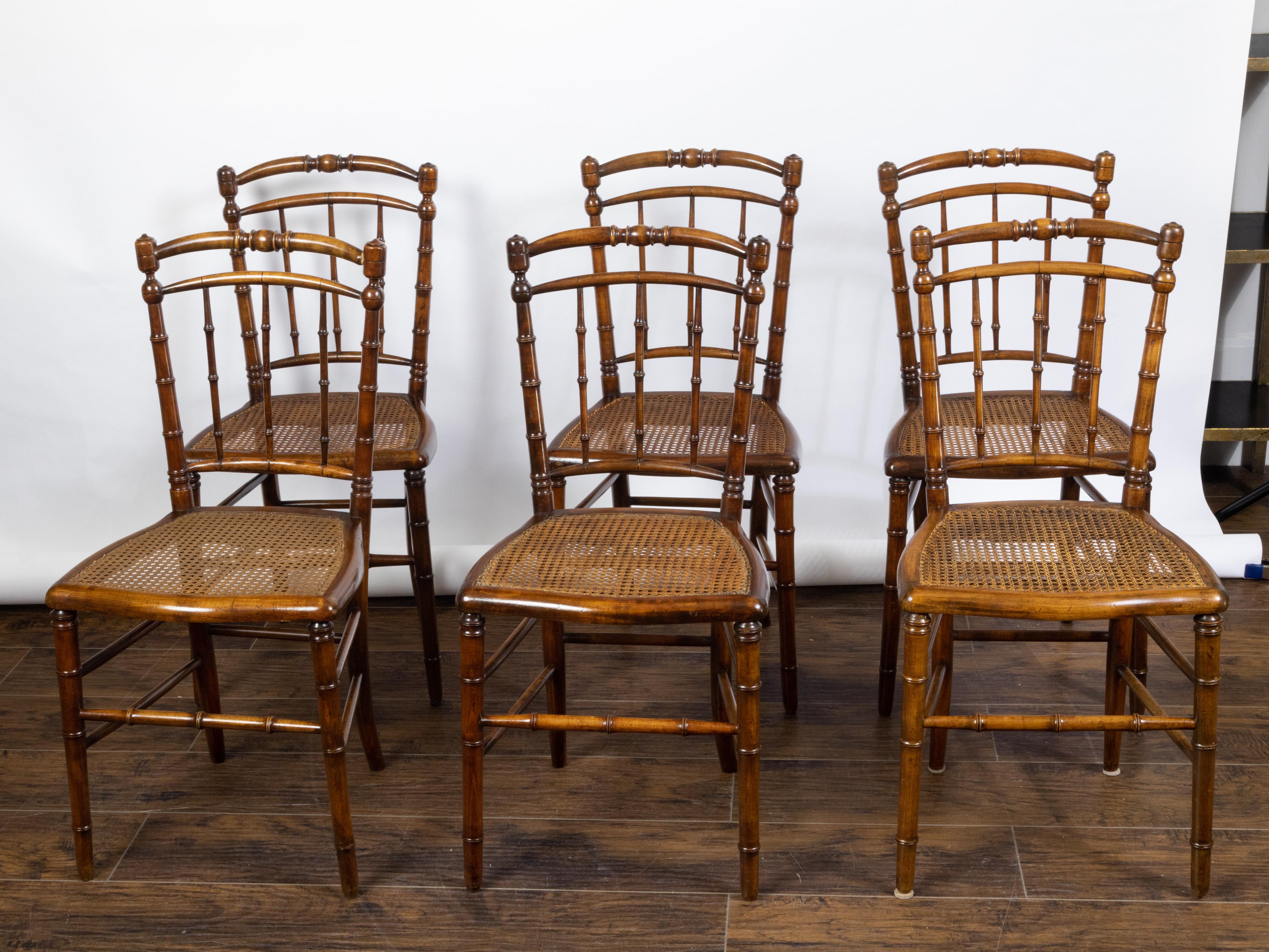 A set of six English faux bamboo walnut side chairs from the early 20th century, with cane seats. Created in England during the Turn of the Century, each of this set of six side chairs features an arching open back flowing seamlessly into the hind