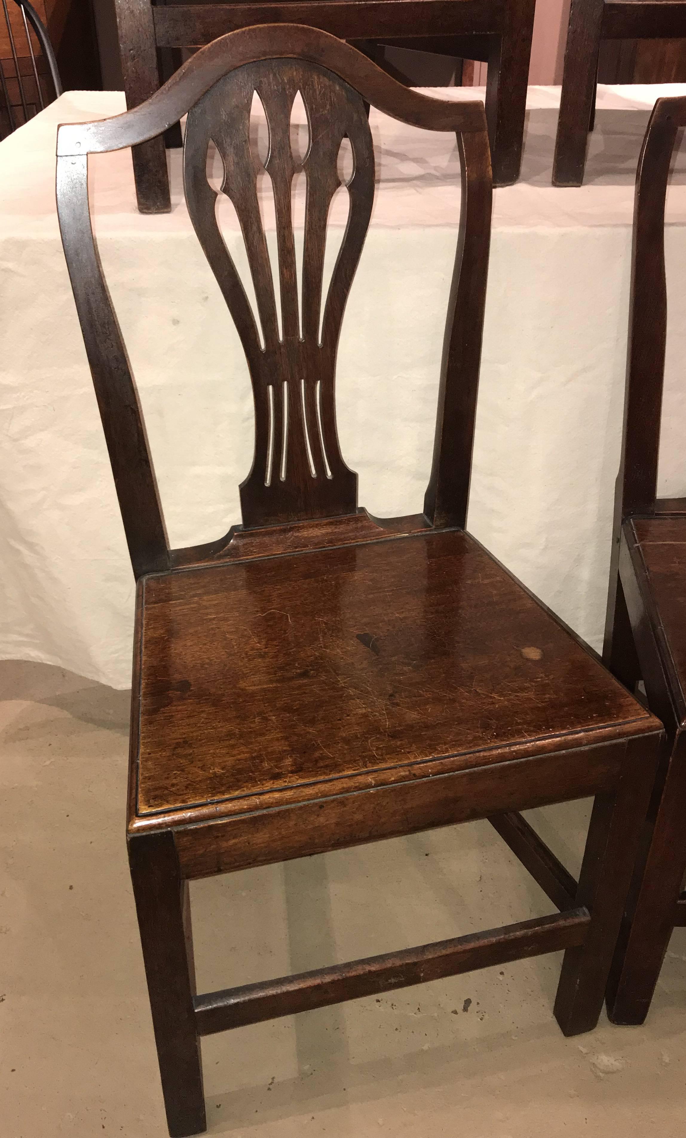 A solid set of six English Georgian oak dining chairs with shaped top rail, flat pierced back splat, simple plank or board seat raised on square legs, with great color. The set probably dates to the late Georgian period (early 19th century) and is