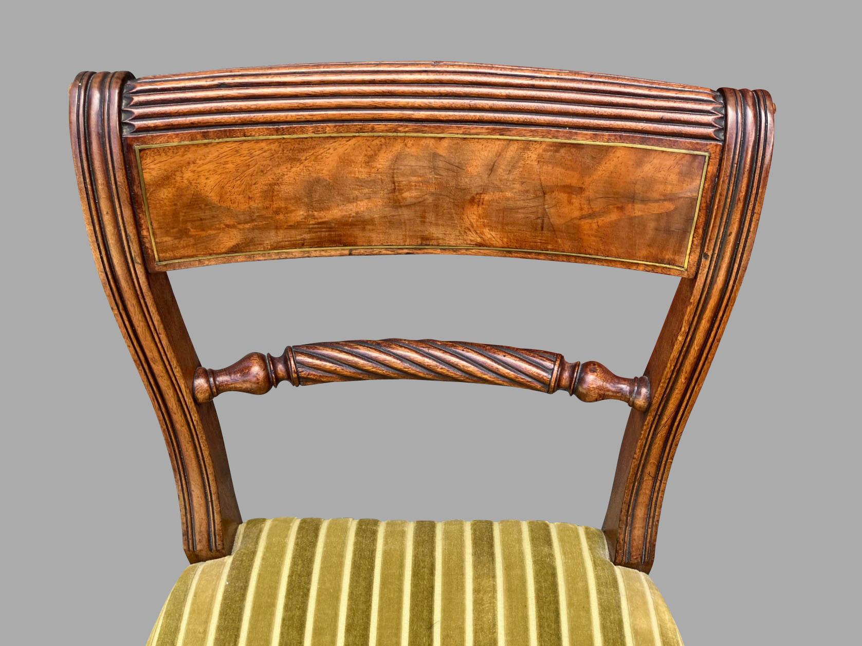 A set of 6 English Regency period side chairs, the top of the curved and reeded back splat inlaid with brass stringing, the lower part with a rope turned central element and supported by reeded stiles with decorated ends. The upholstered seats are