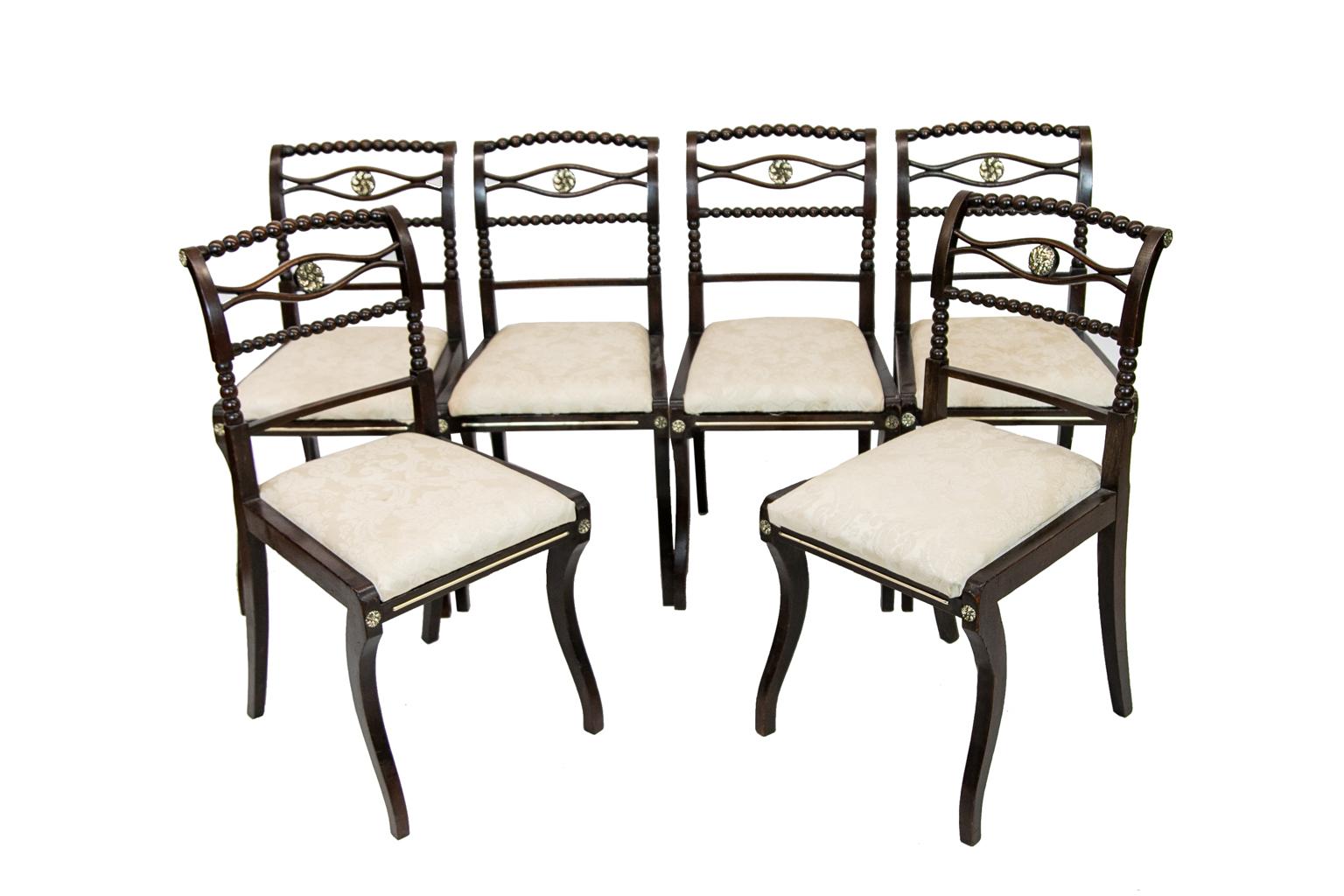 Set of six English Regency side chairs are fruitwood with floral brass medallions in the center cross splat. Each has bobbin turned crest rail, cross splat, and stiles. The front legs are ogee shaped and there are brass ray inlaid in the front