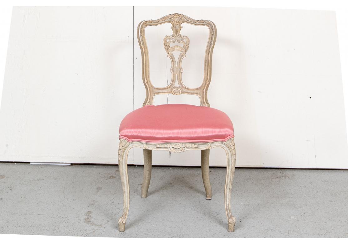 Elegant Louis XV style with overall carved details in a greige paint. The shaped crest rails with acanthus leaves and the splats with scrolled shell motifs. Ribbon carved skirt and floral carved cabriole legs. The comfortable shaped seats