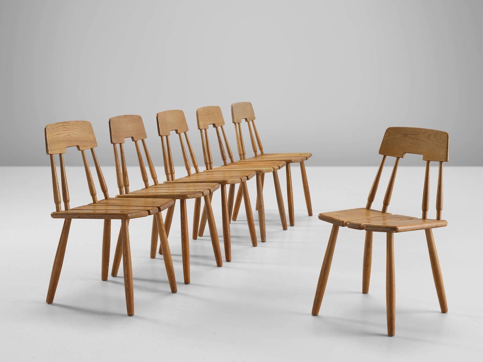 Set of six dining chairs, oak, Finland, 1950s.

This set of six chairs in solid oak features elegant details in the back. The seating consist of three slats and is detailed with wood-joints of the four legs. Four cylindrical bars with one horizontal