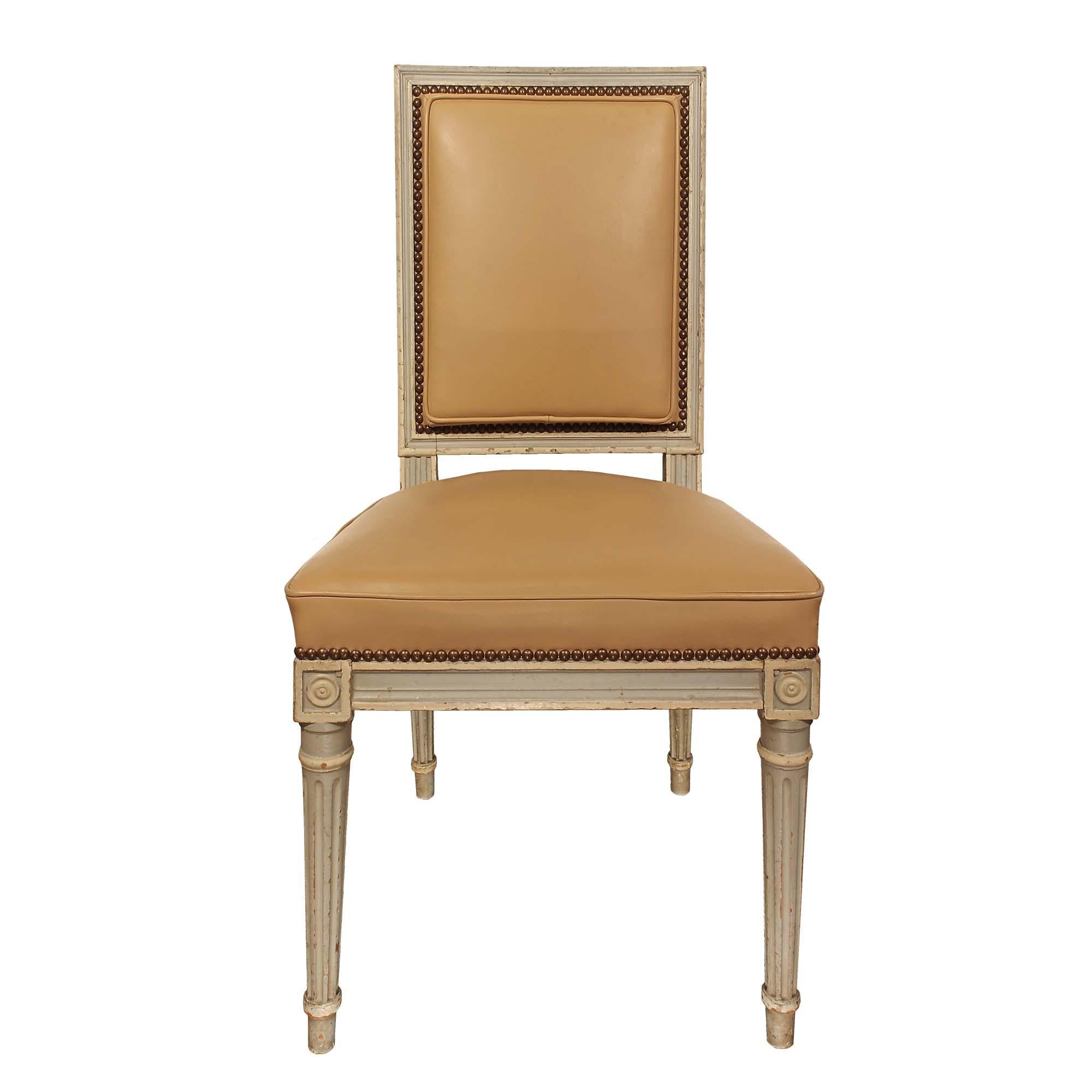 A striking set of six French 19th century Louis XVI st. patinated dining chairs. Each chair is raised by four slender circular tapered fluted legs with block rosettes at each corner. The seat and back support are upholstered in a beige leather, with