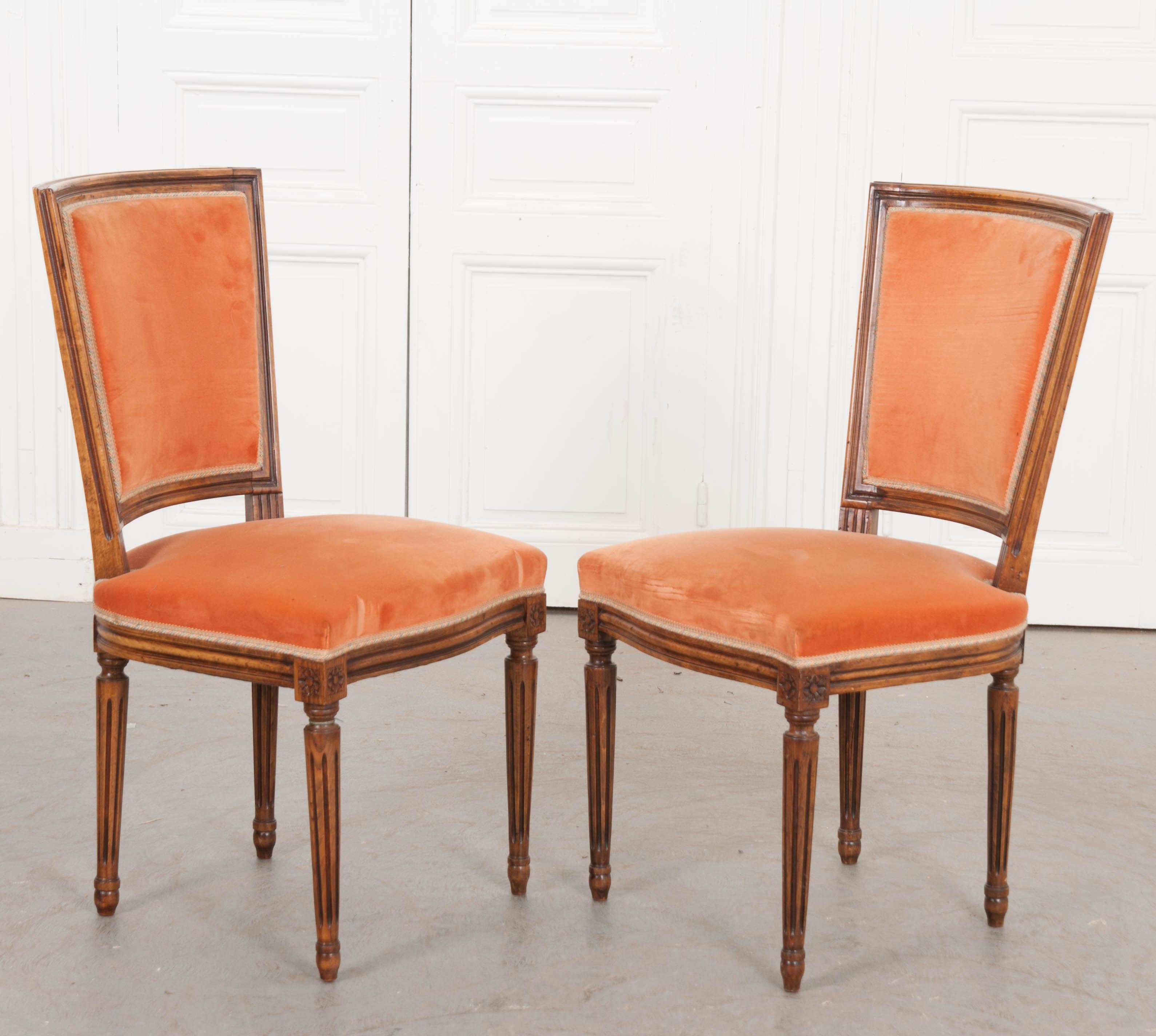 This great set of six Louis XVI style walnut side chairs, circa 1880, are from France and have rectangular tapering backs with fluted carving throughout. They are upholstered in a rich peach velvet.