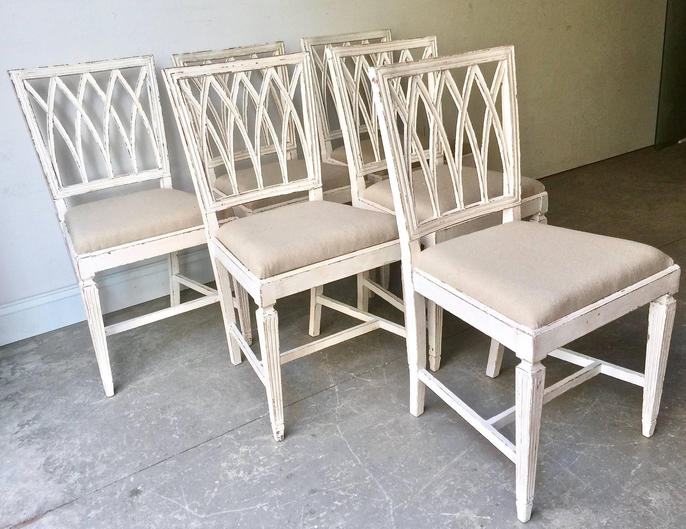 A charming set of six of French late 19th century painted side chairs with richly carved open lattice backs, loose upholstered seats in linen and fluted tapered legs with H-stretchers in time worn cream-white patina. France, 19th