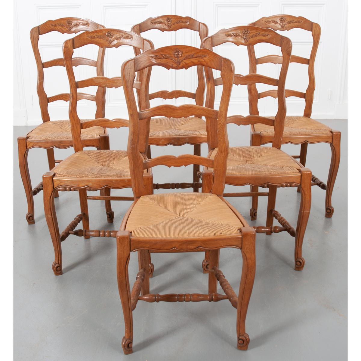 This lovely set of six, vintage, Louis XV-style fruitwood dining chairs, circa 1940s, is from France and feature floral-carved ladder backs, rush seats, cabriole legs with turned stretchers and escargot feet. The rush seats are removable.