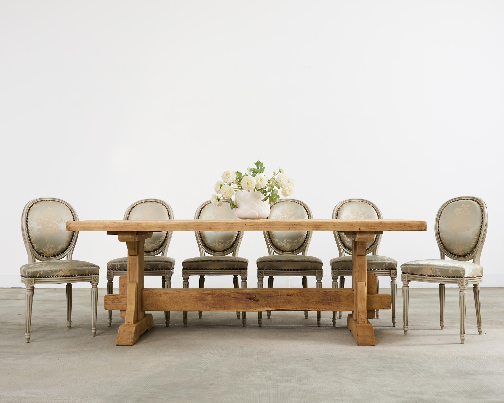 Sublime set of six French 20th century carved beech dining chairs crafted in the grand Louis XVI taste. The oval balloon back or cameo frames feature an opulent silver cloud or oyster lacquer finish with a desirable aged patina. The painted finish