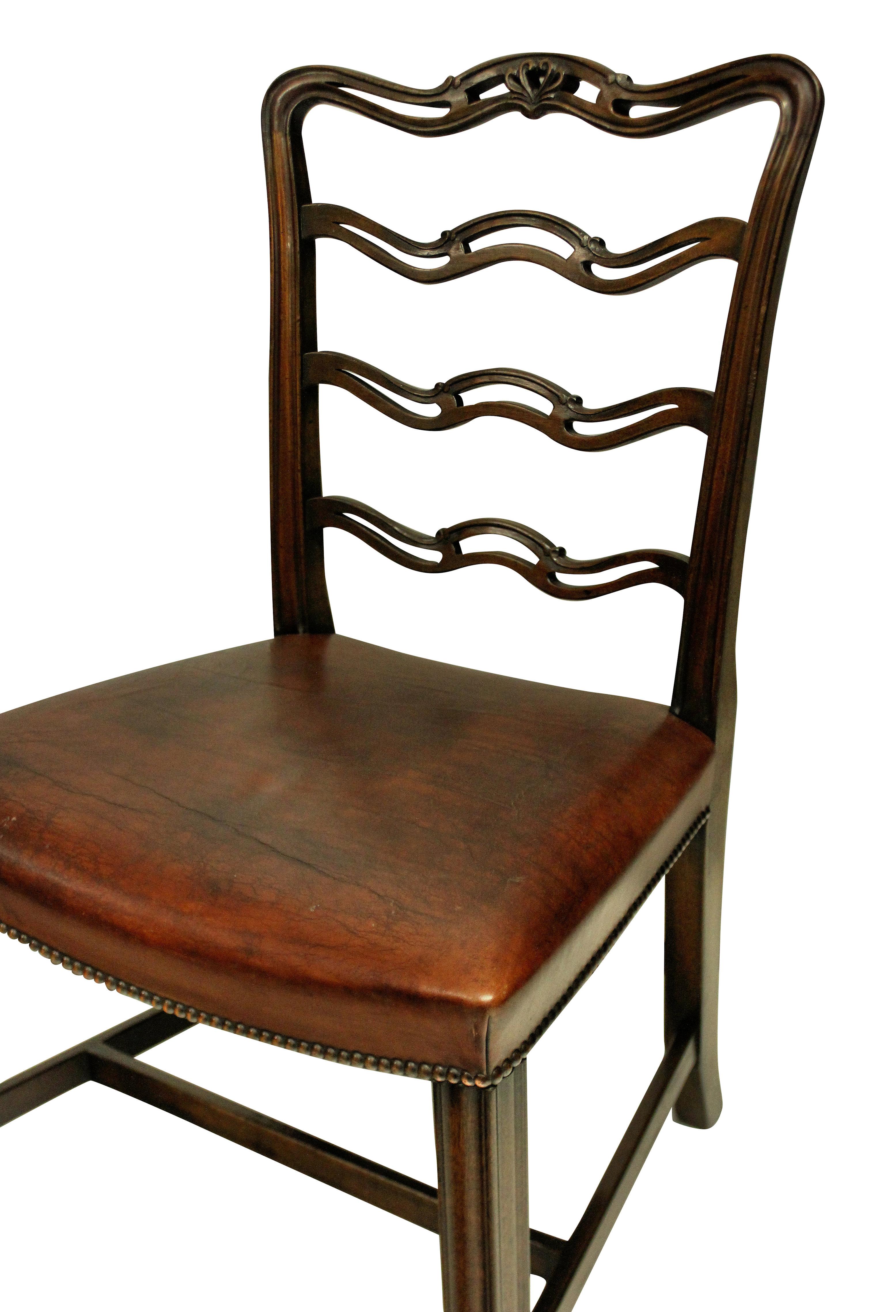 A set of six George III style mahogany ladder back dining chairs with the concave seats upholstered in leather with stud detail.