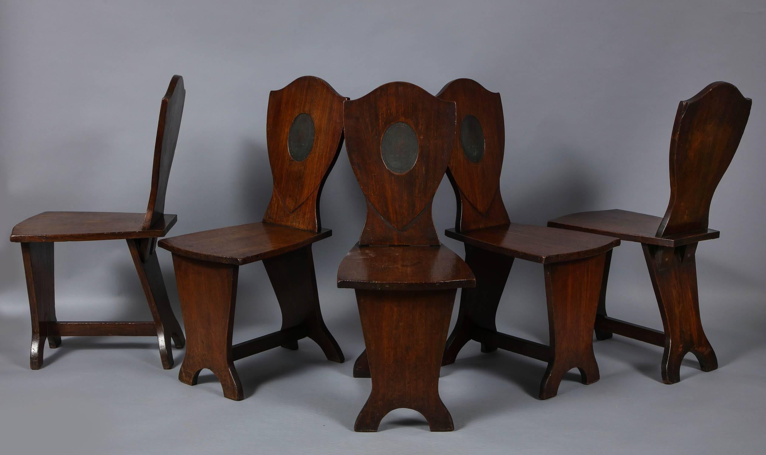 Fine set of six George III period mahogany hall chairs, the shield shaped backs with inset painted heraldic devices, on plank seats, the trestle bases with arched silhouette feet joined by cross brace, the whole with good rich color and